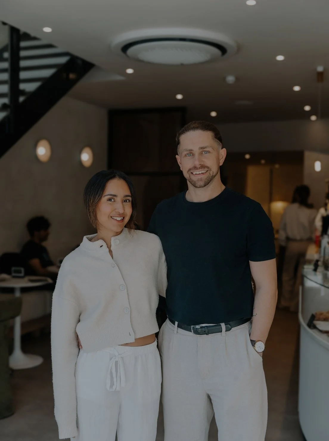 A man and a woman standing together inside a modern, well-lit restaurant or cafe, smiling at the camera.