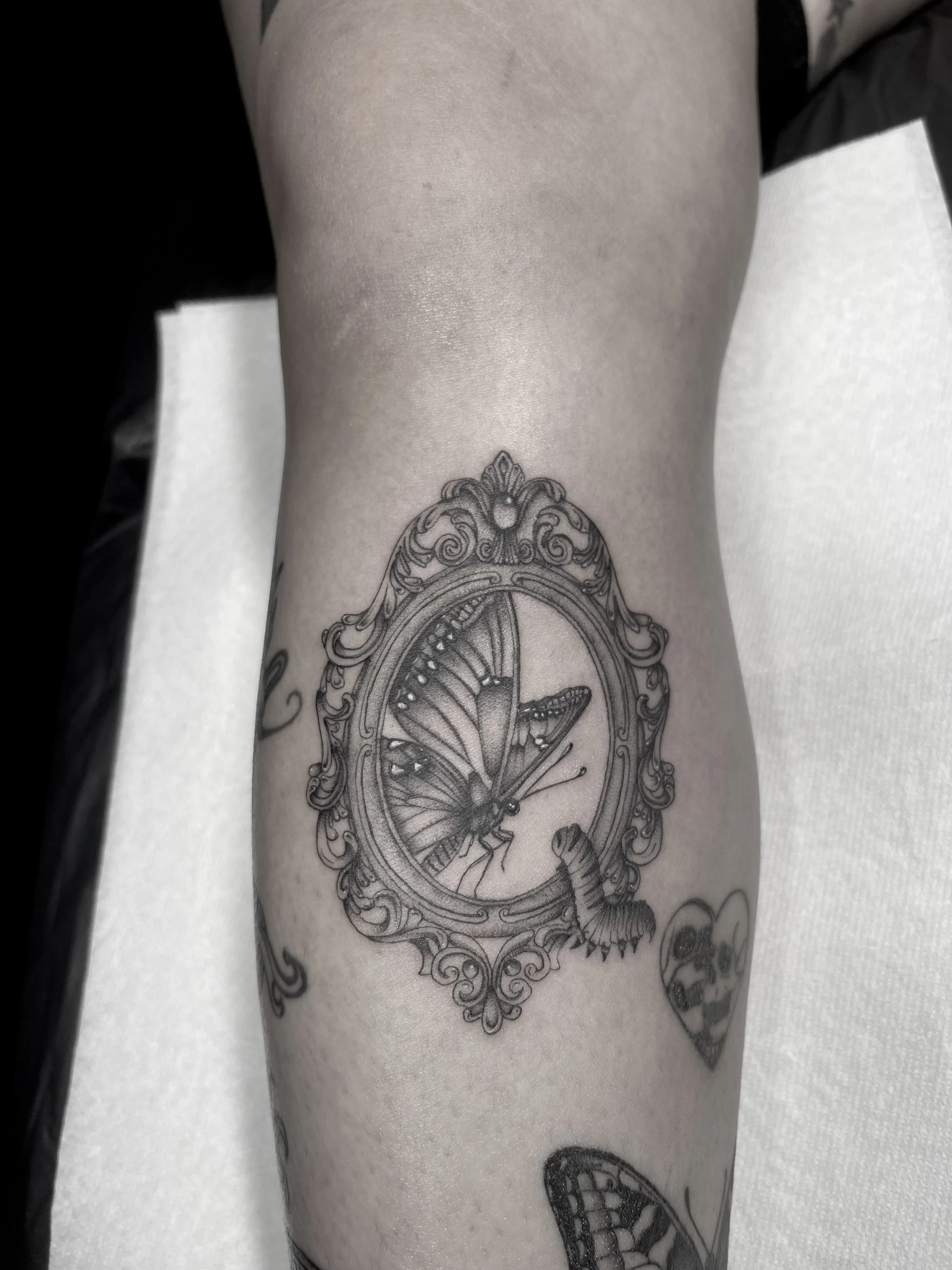 Close-up of a person's arm with a black and gray tattoo of a clock with a butterfly inside it.