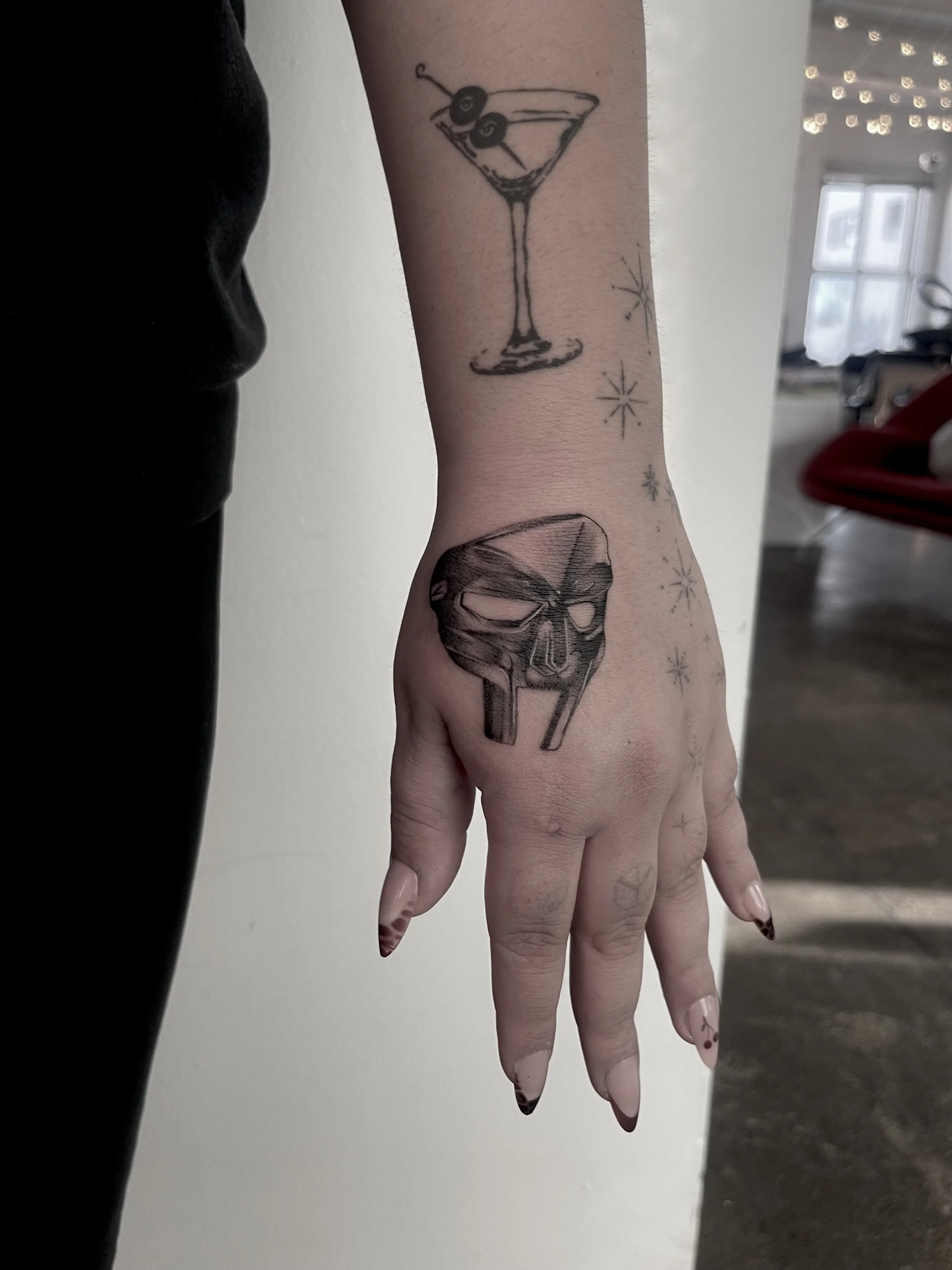 Tattoo of a cocktail glass with olives and a small skull tattoo on the wrist, with starburst designs around.