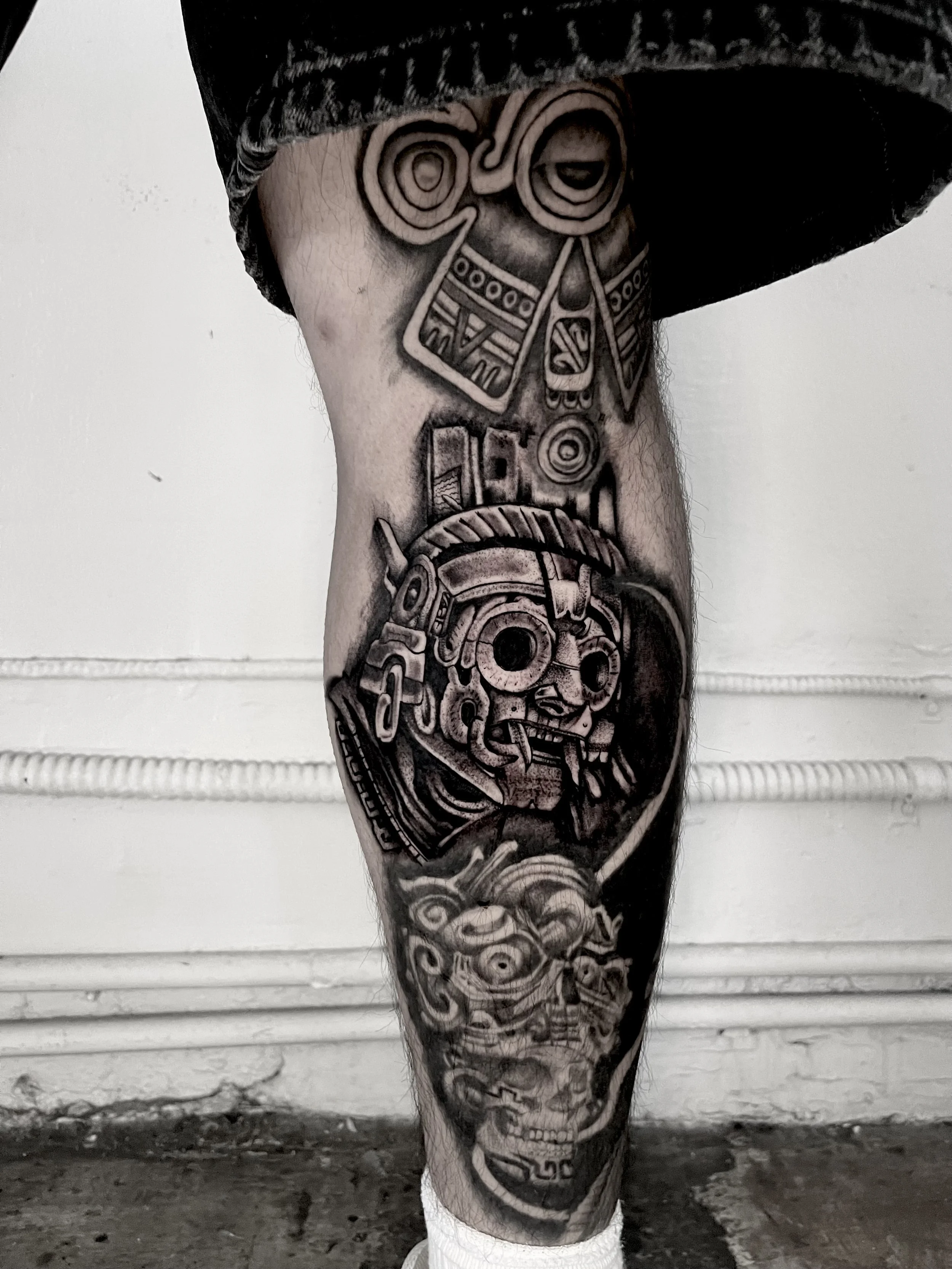 Black and gray tattoo sleeve on a person's leg featuring a skull, mechanical gears, and abstract patterns.