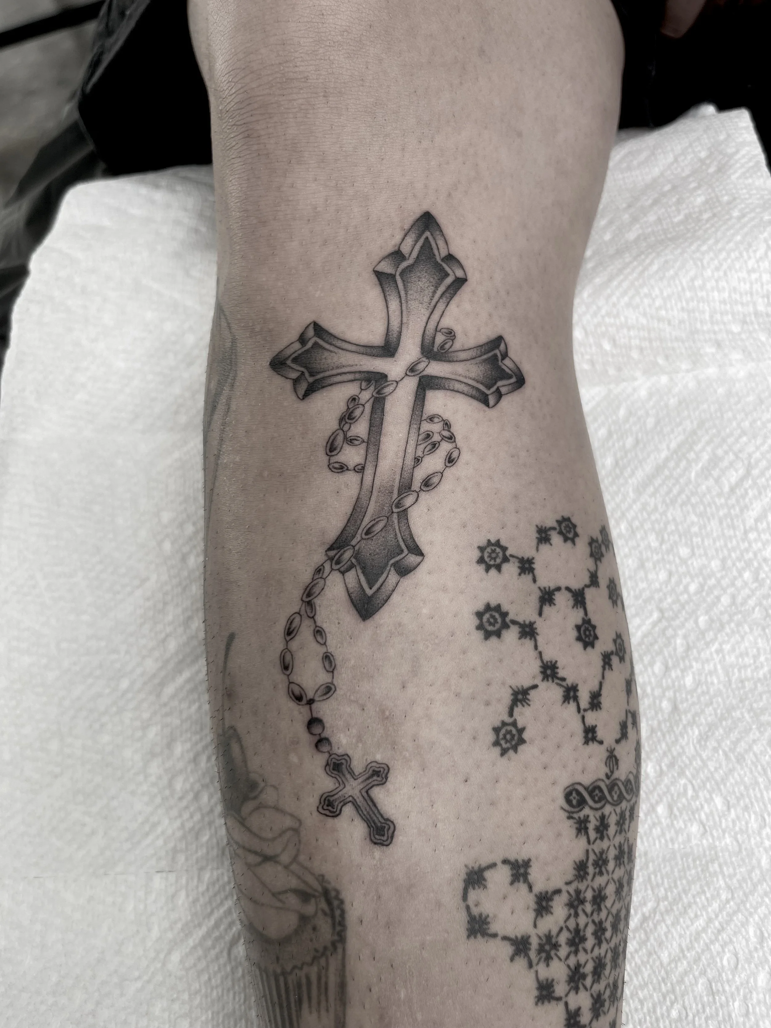 Tattoo of a cross with decorative elements on a person's arm.