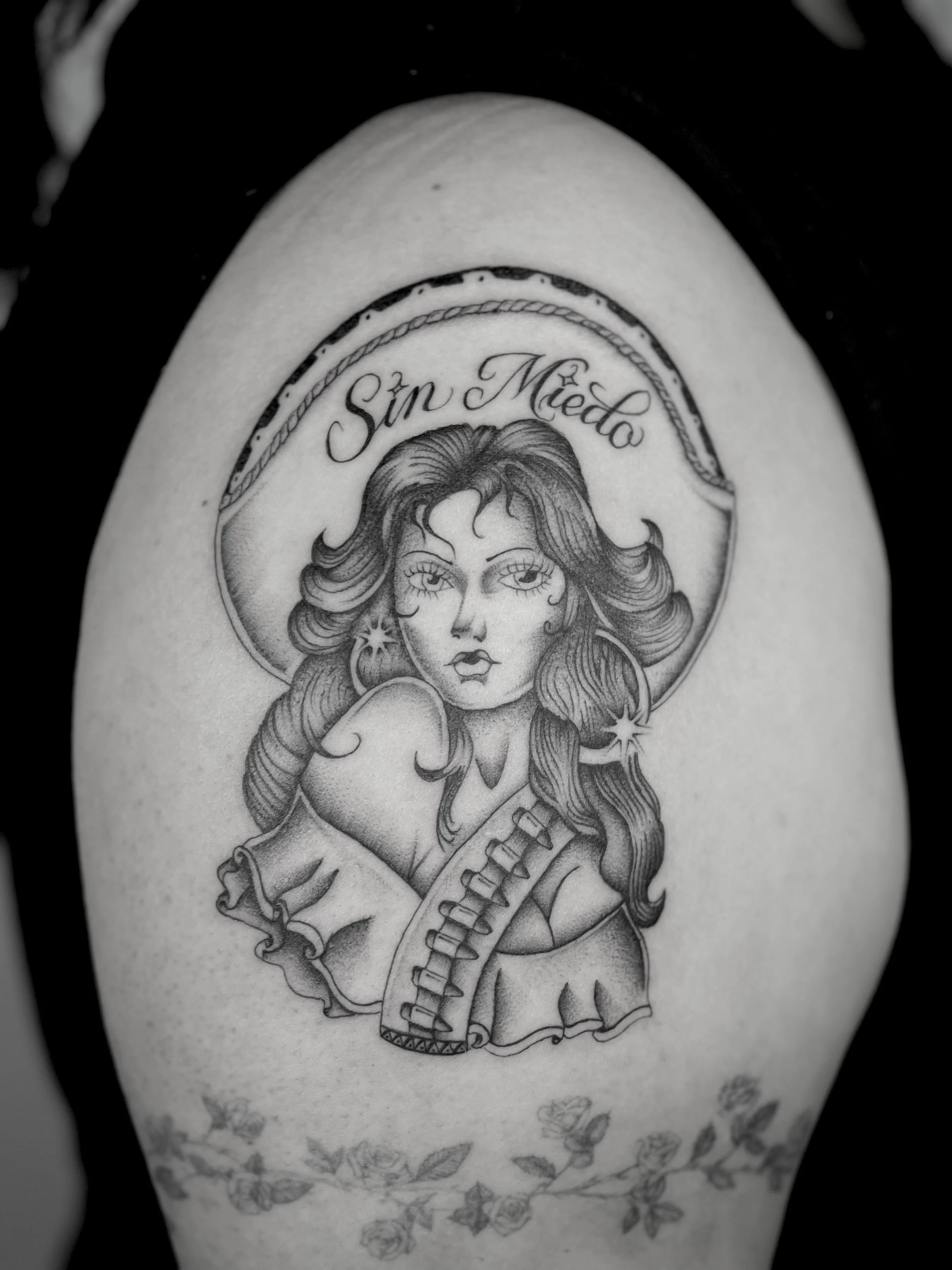 Black and gray tattoo of a chicano woman with flowing hair, angel wings, and the words 'Sin Miedo' above her head.