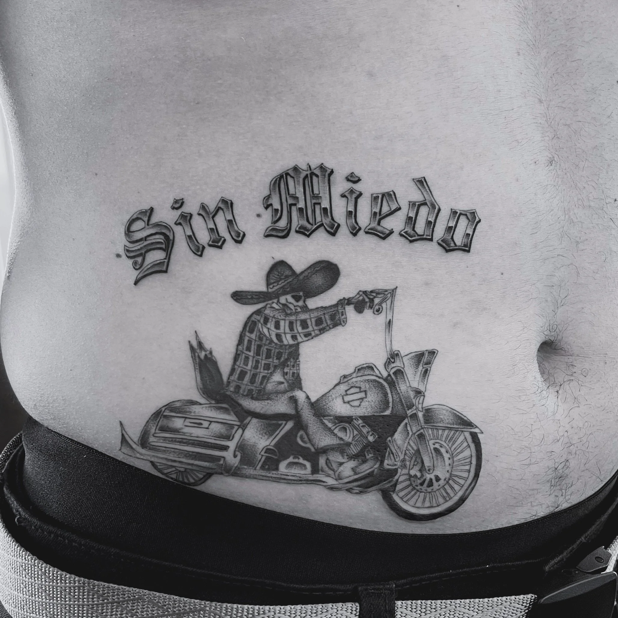 Close-up of a zipper on a piece of clothing with a tattoo visible underneath, featuring stylized gothic lettering and a cartoon-style snake illustration.