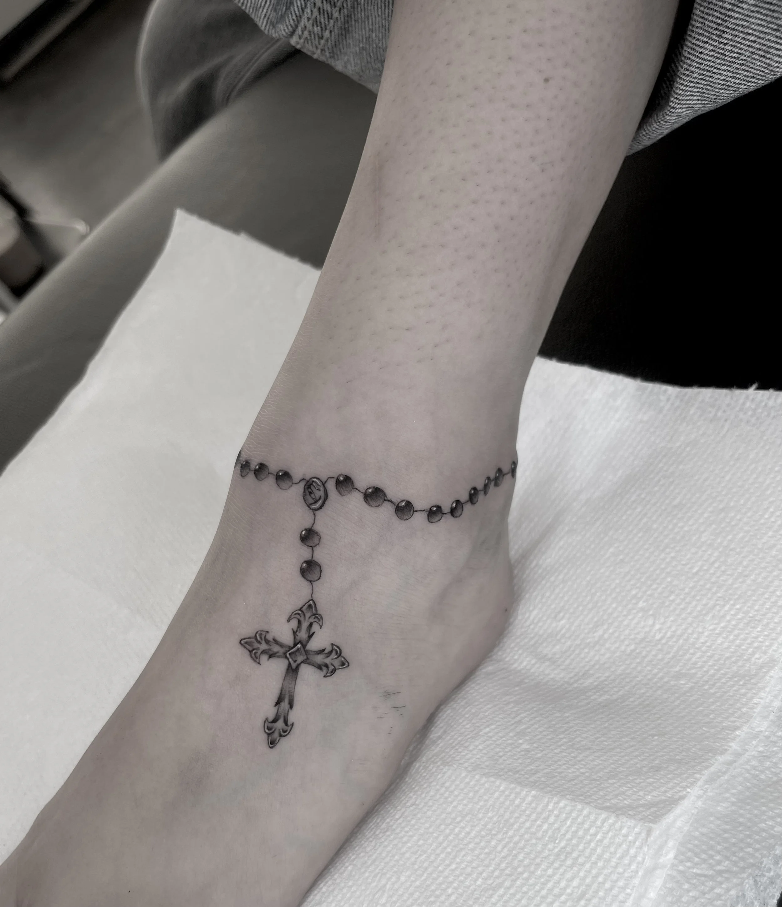 Tattoo of a cross with floral details on a person's forearm, with a beaded bracelet around the wrist.