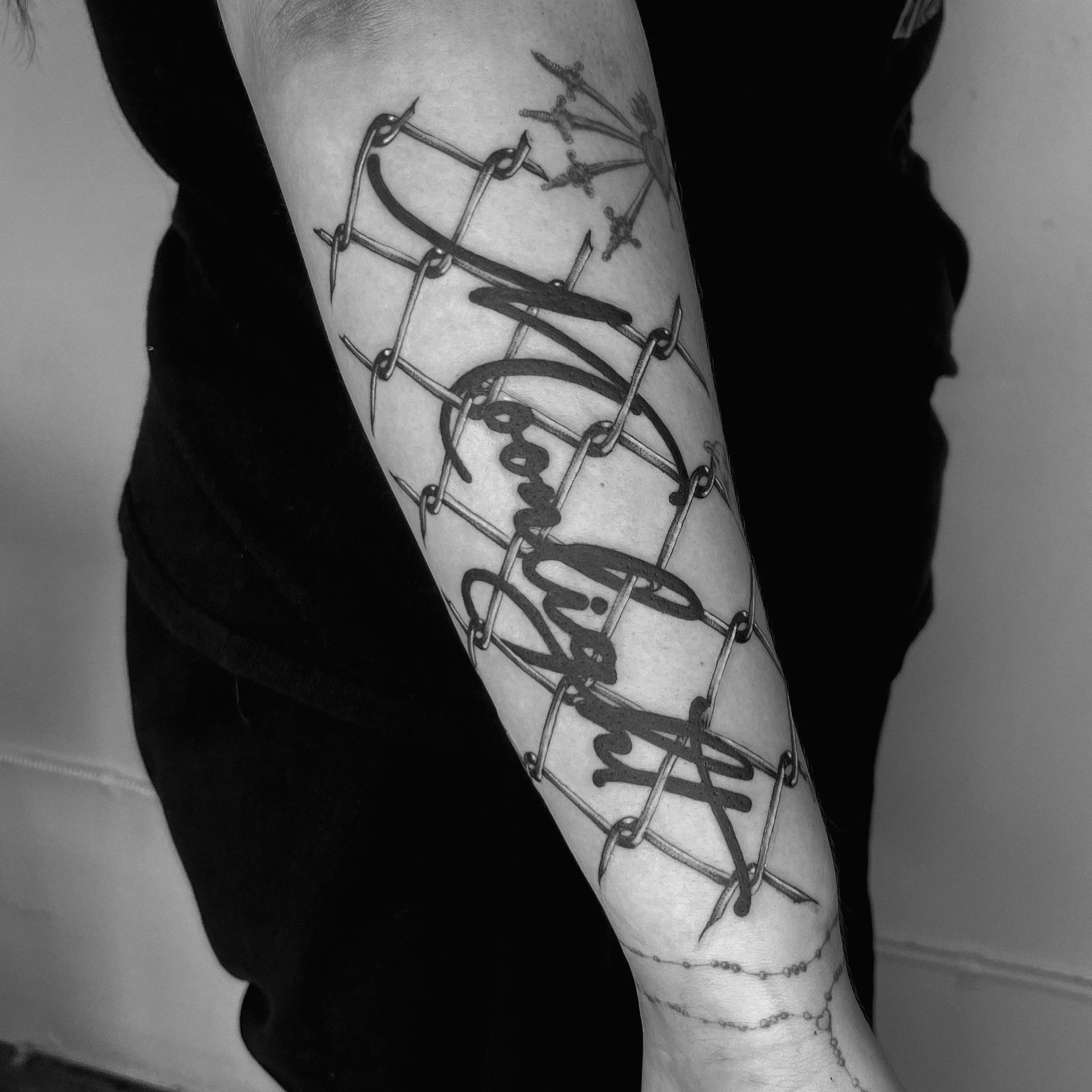 Black and white photo of a person's arm with multiple tattoos, including a detailed clock face, swords, and chains.