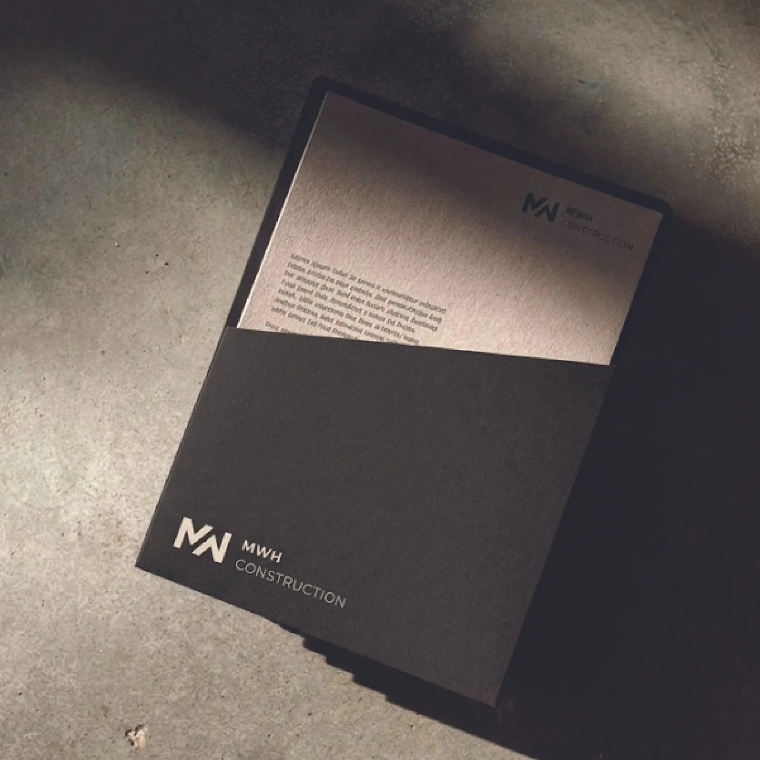 Close-up of a black sign on the ground with white text reading 'MN MWASH CONSTRUCTION,' with a concrete sidewalk surface around it.