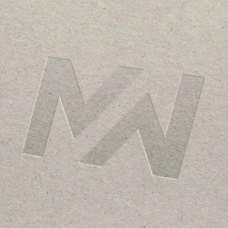 Close-up of an embossed letter 'W' on a textured beige paper.