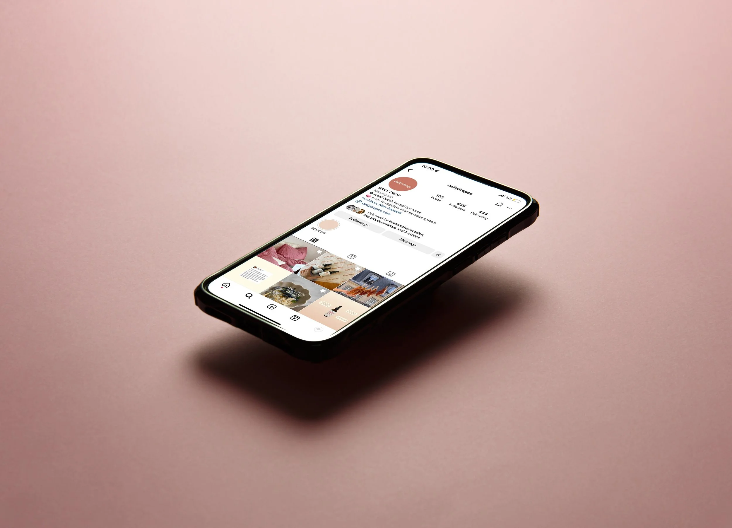 A smartphone lying on a pink surface screen displaying an Instagram profile page.
