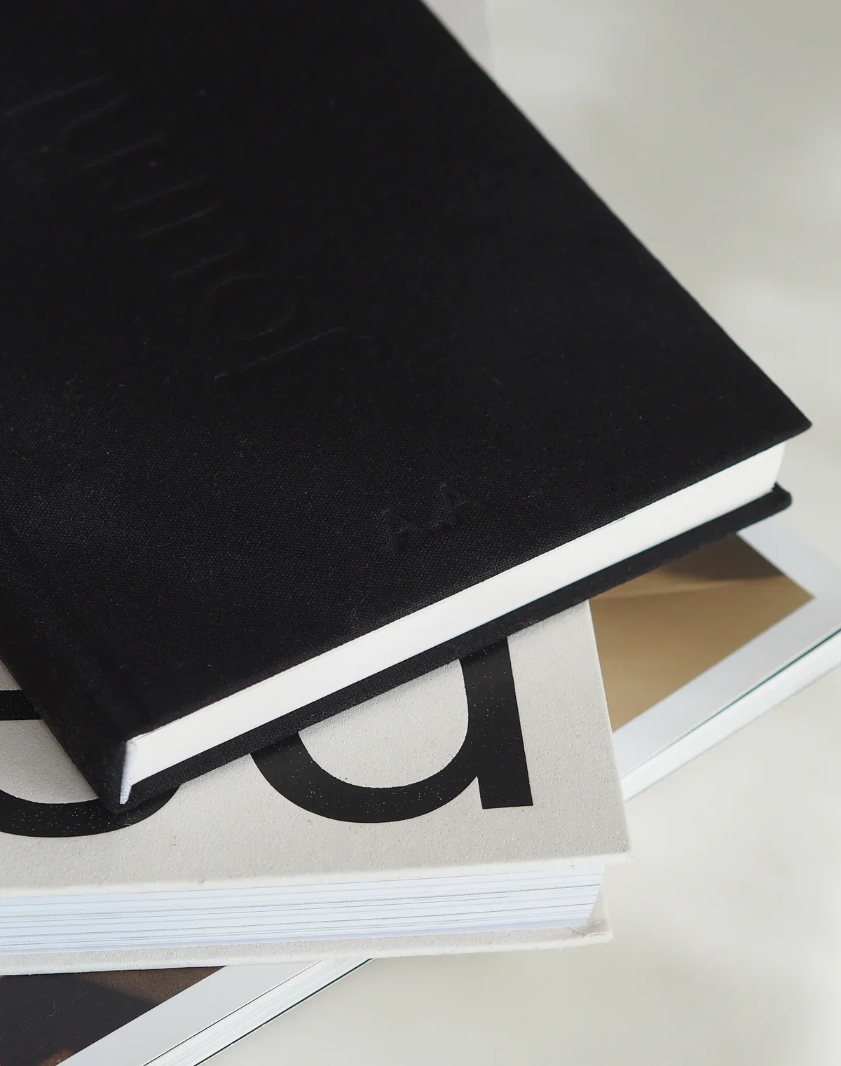Close-up of black book with embossed logo resting on a white bag with large black letters, placed on a white surface.