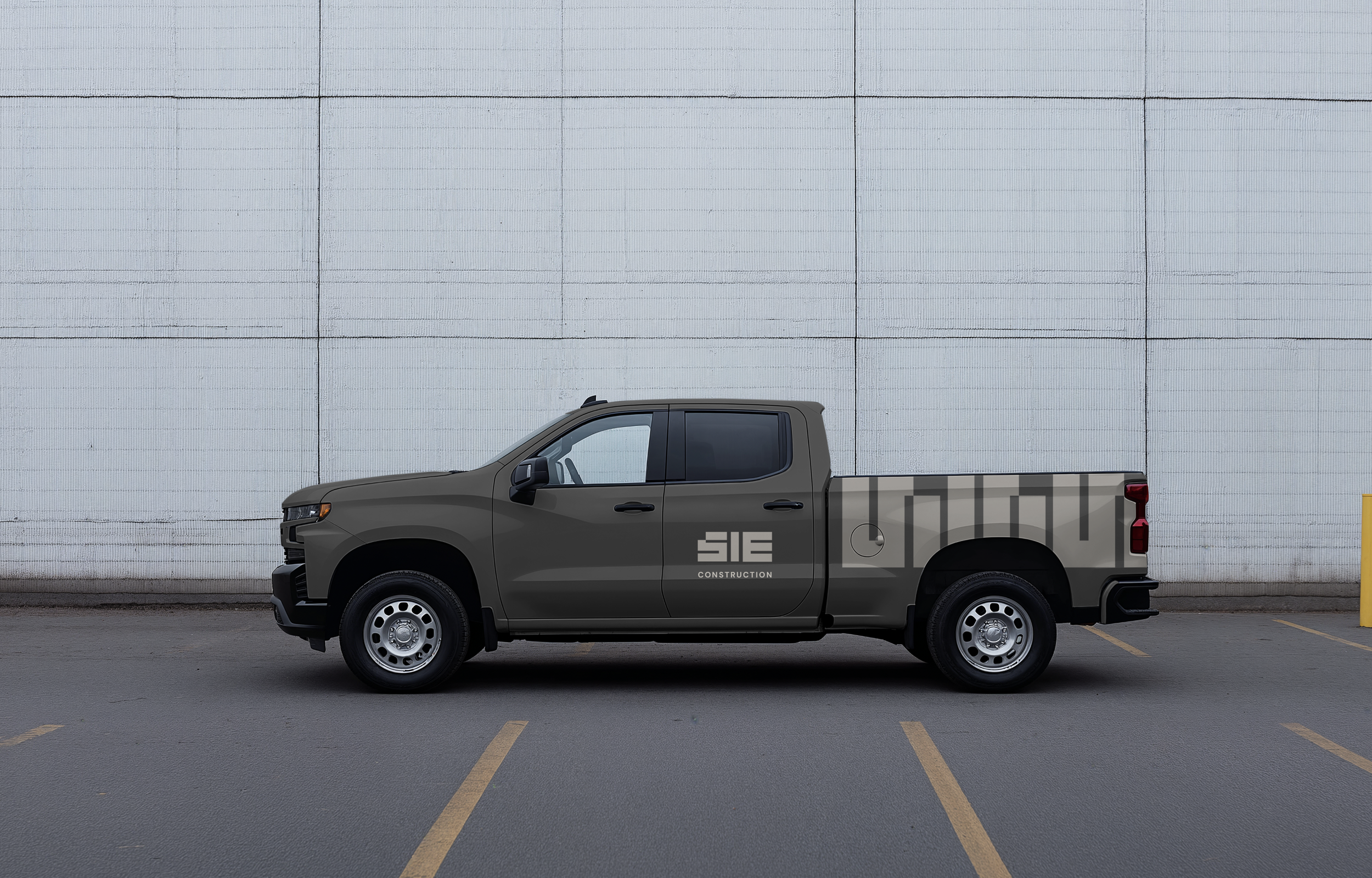 Gray pickup truck parked in an empty parking lot against a white concrete wall.