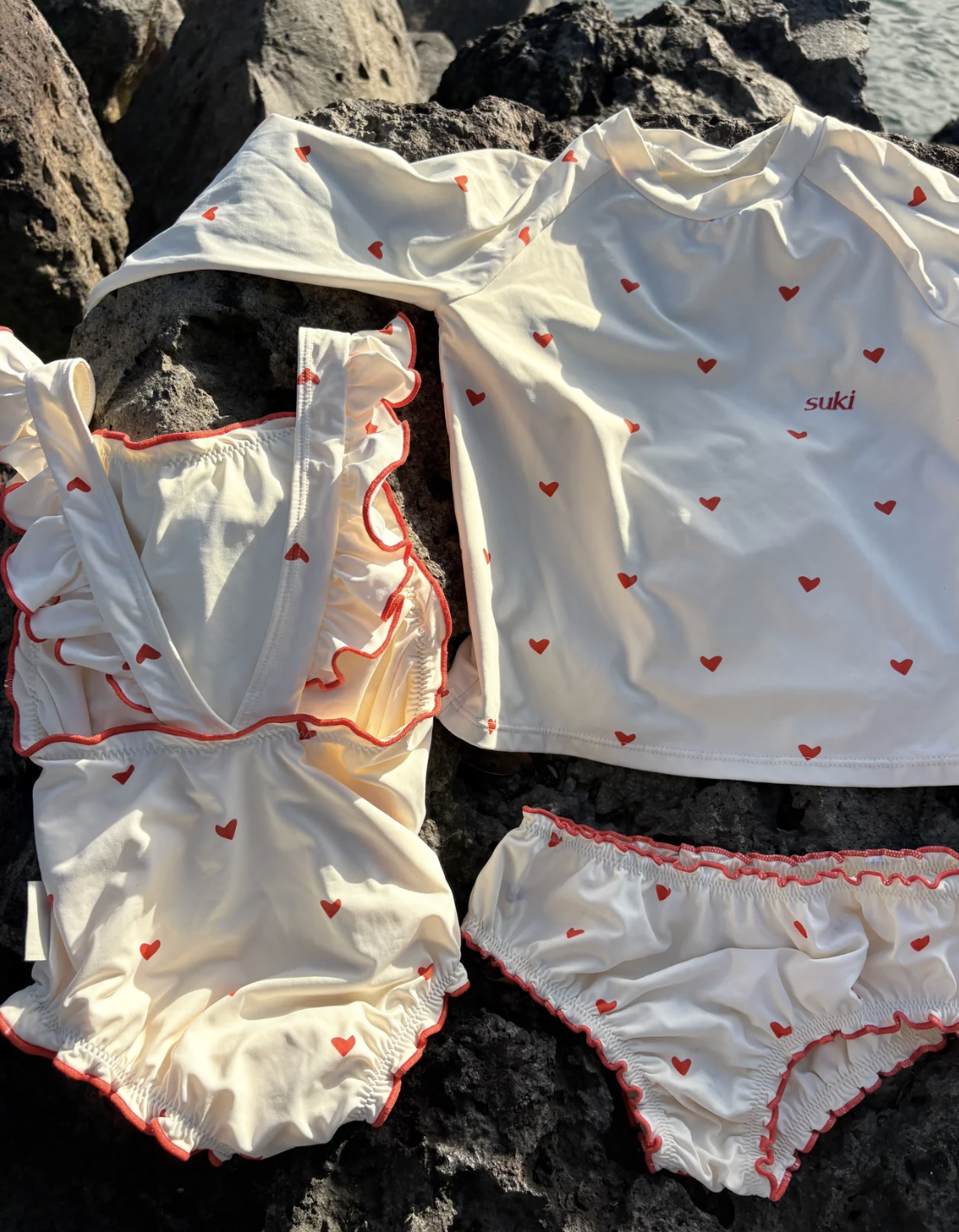 A white swimsuit with red heart patterns laid out on rocks outdoors