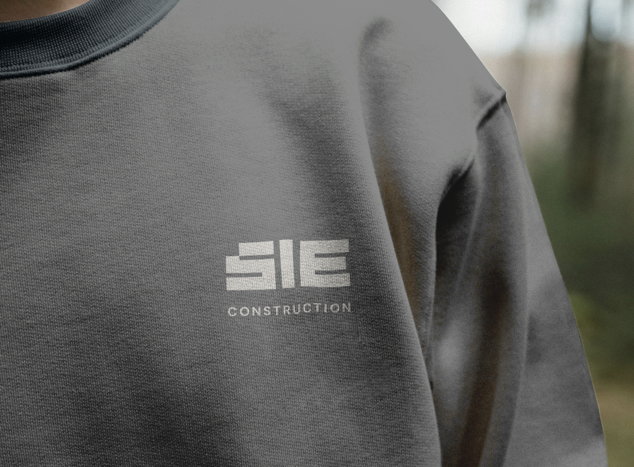 Close-up of a grey construction worker's shirt with the logo 'SIE CONSTRUCTION' printed on the chest.