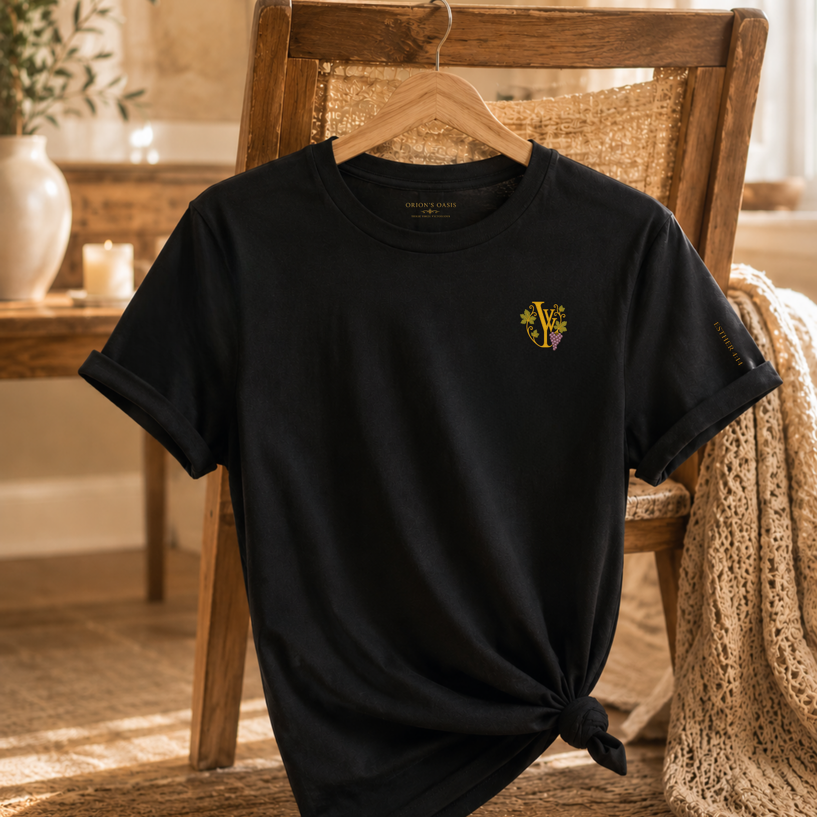 Black T-shirt hanging on a wooden chair, with a logo featuring a grape cluster and the letters V and J, with the text 'Orion's Oasis' inside the collar.