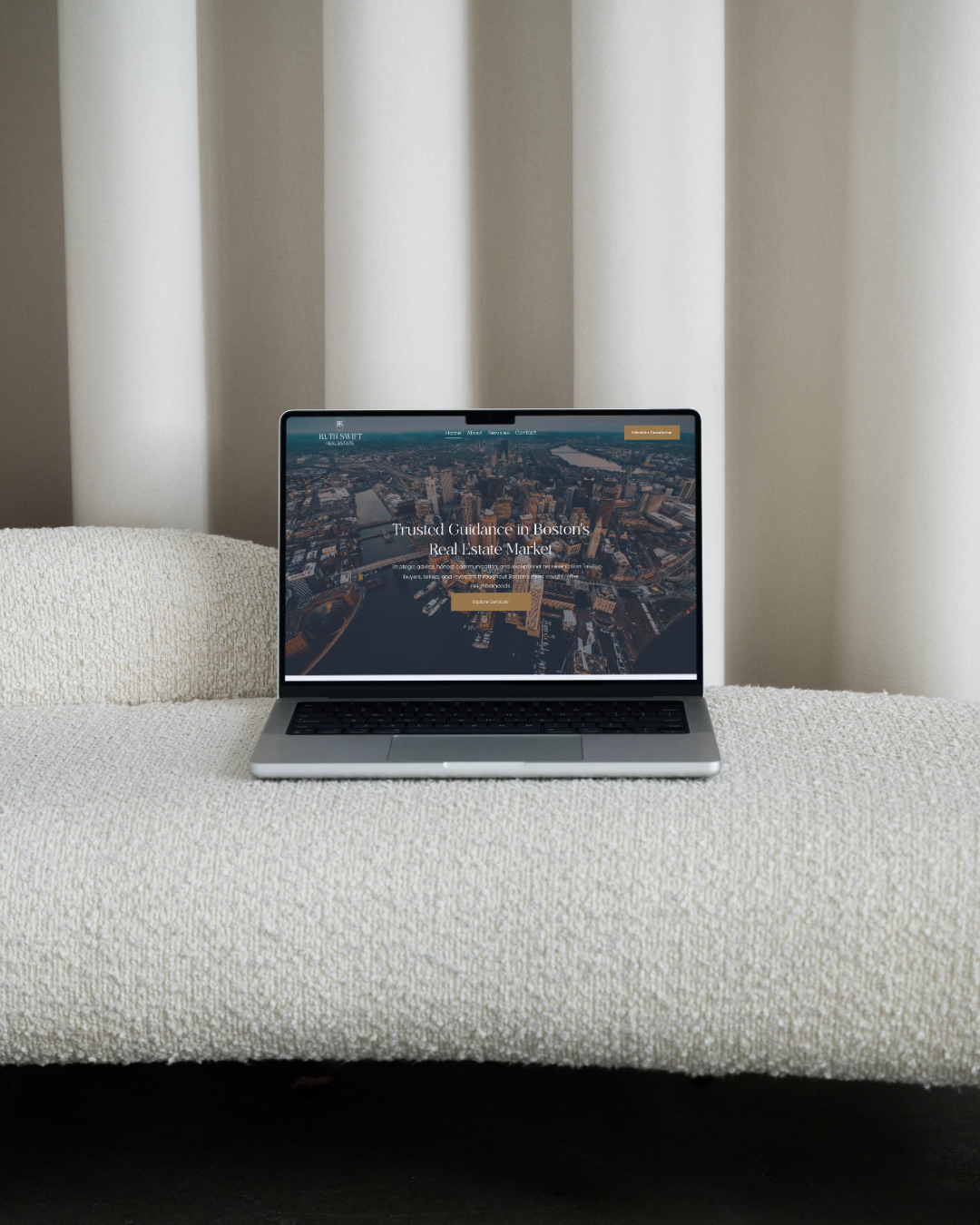 Laptop displaying a Boston real estate website on a white textured couch