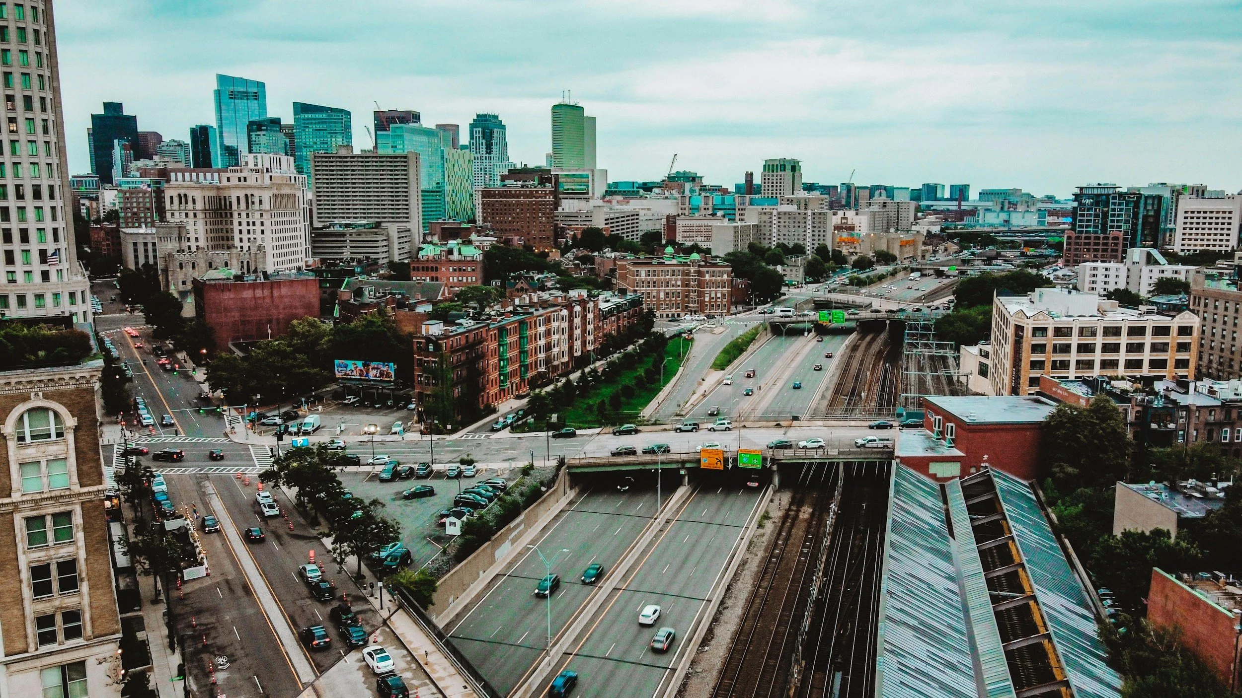Aerial view of a downtown city skyline with high-rise buildings, busy highways, and railroad tracks under an overcast sky.