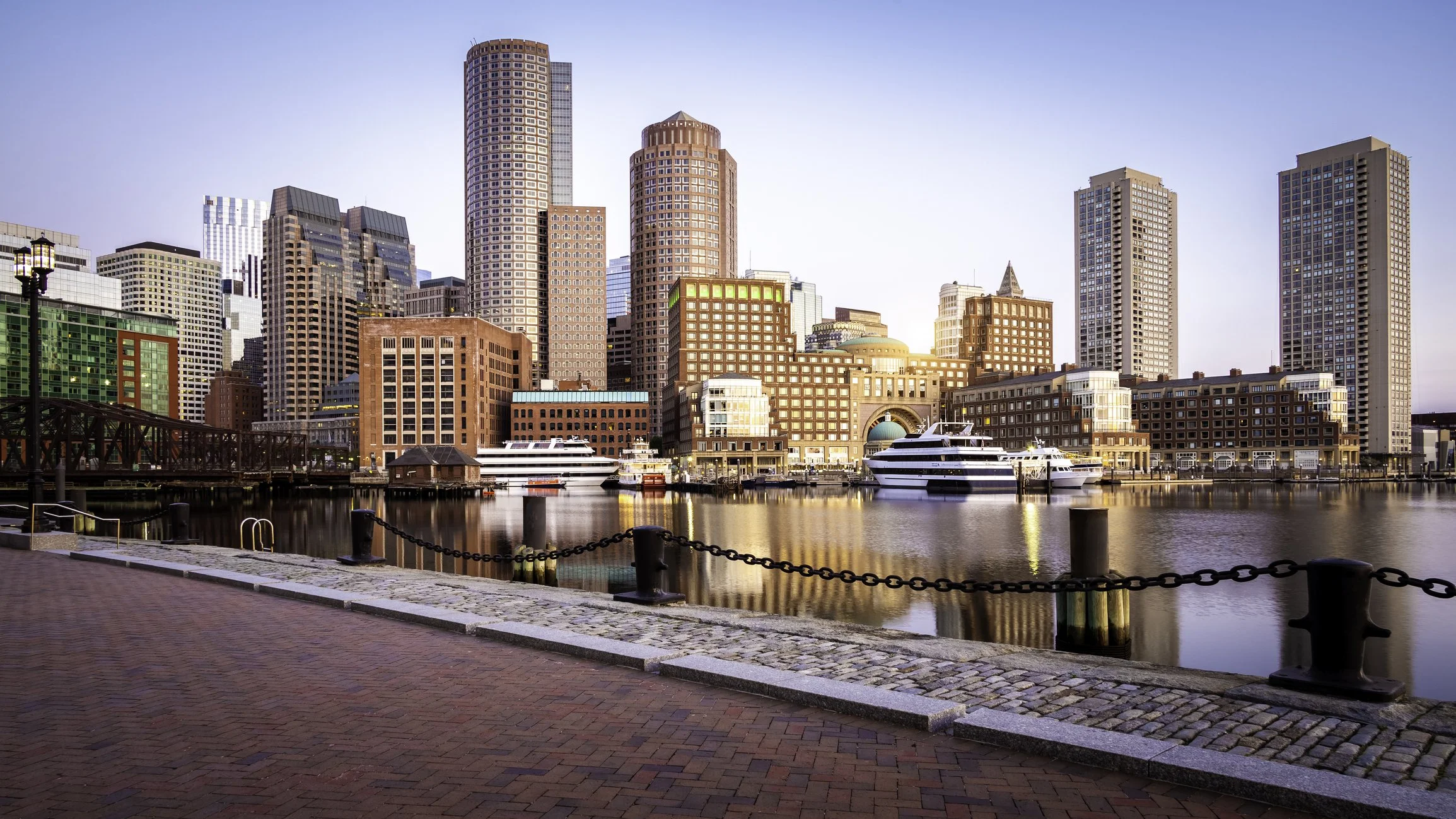 Boston waterfront skyline with skyscrapers, boats, and historic harbor buildings at sunset