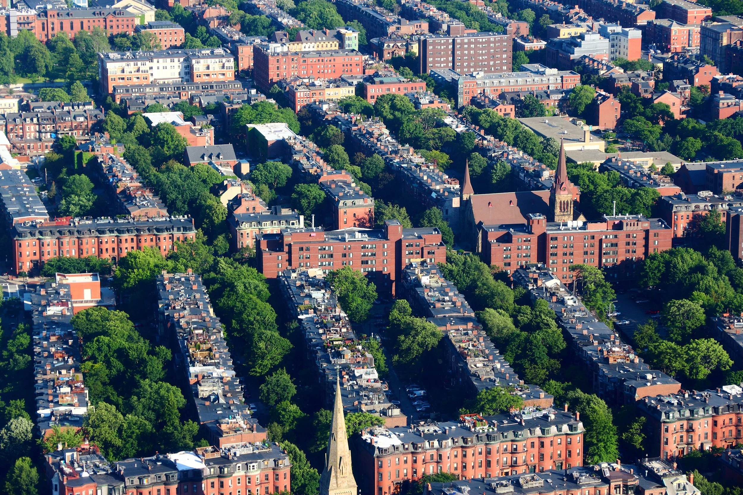 Aerial view of Boston’s historic Back Bay neighborhood, showing dense red-brick buildings, tree-lined streets, and church spires.