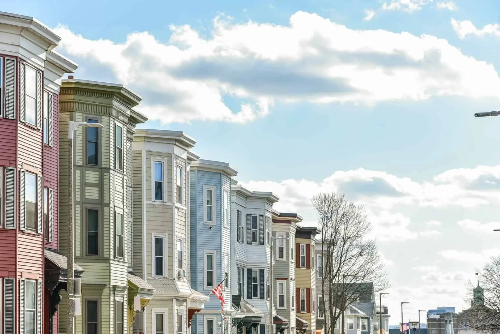 Colorful historic row houses lining a city street beneath a bright, cloud-filled sky