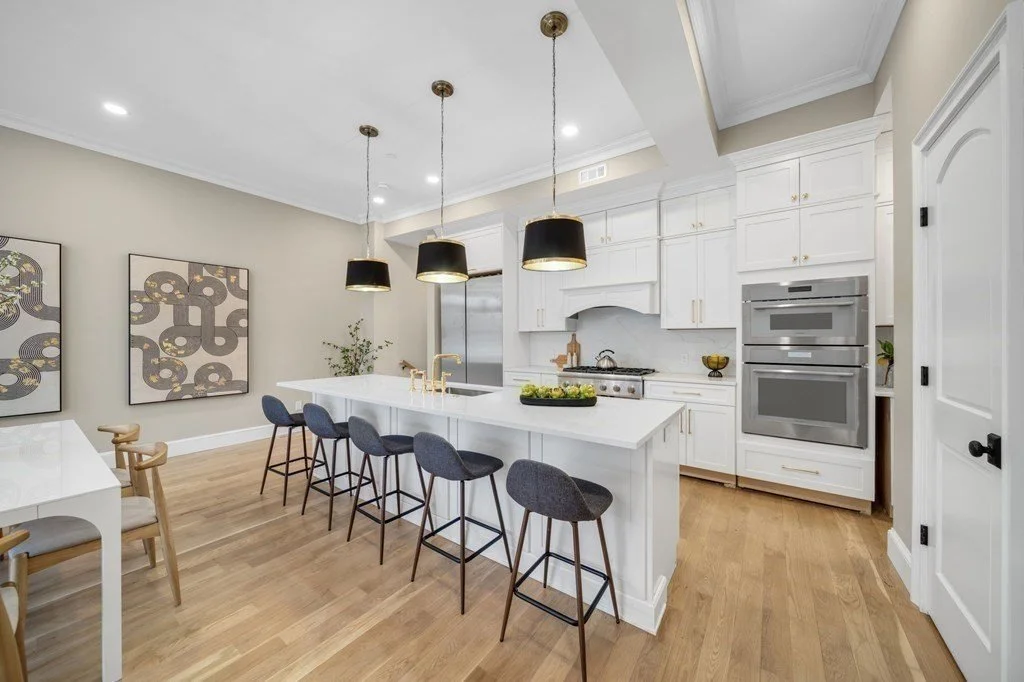 Modern white kitchen with island seating, pendant lights, double ovens, and hardwood floors