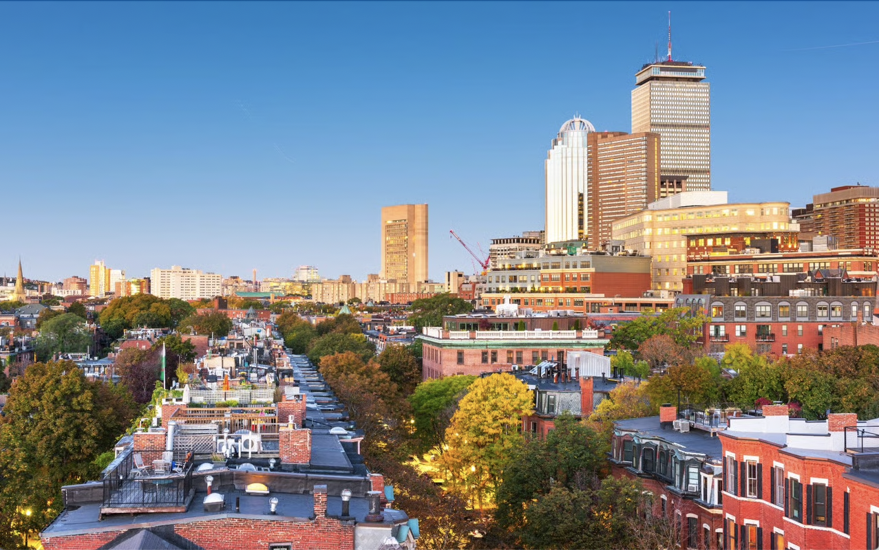 Boston skyline at sunset with historic brownstones, colorful autumn trees, and the Prudential Center tower