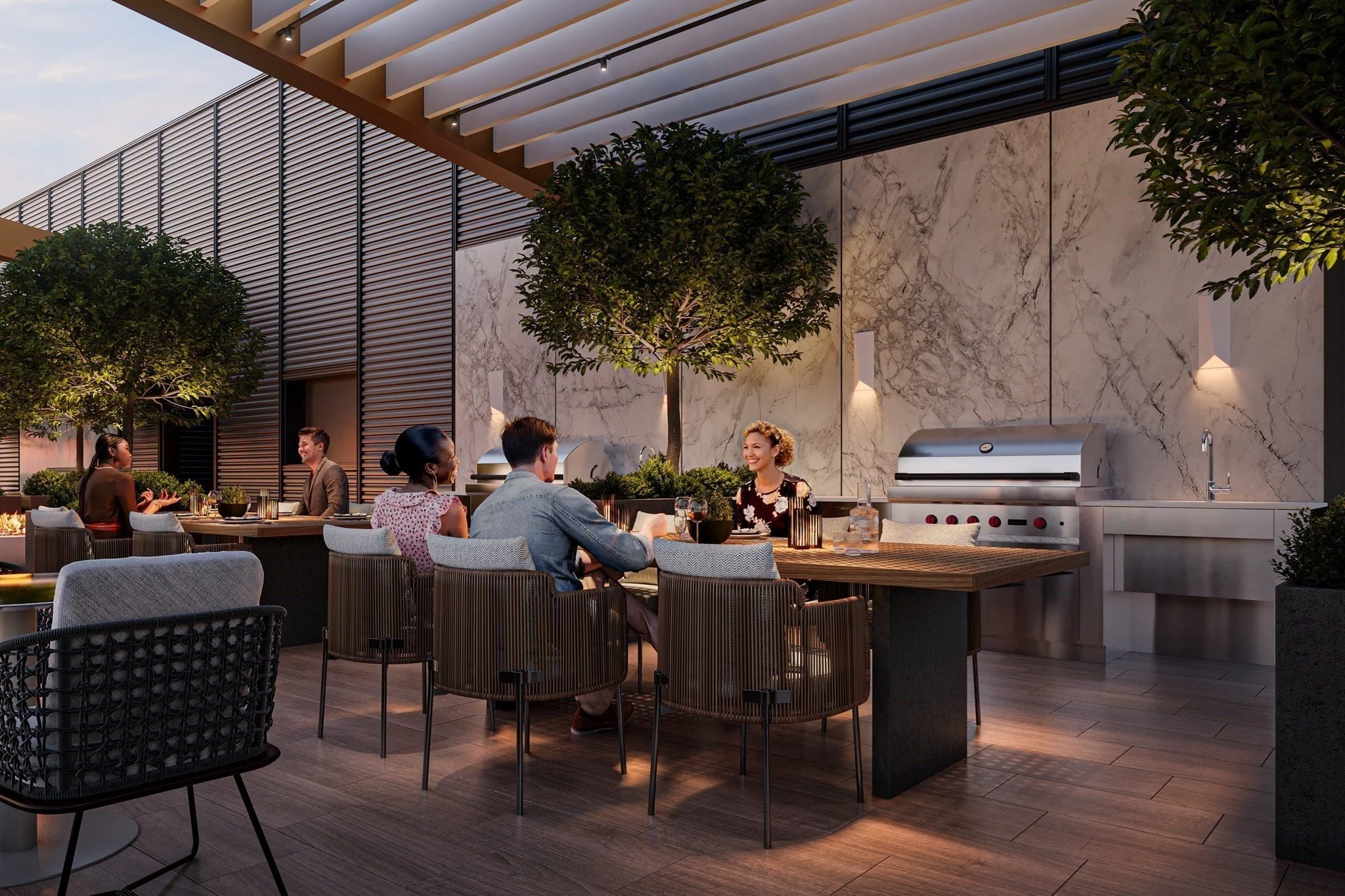 People dining at tables in a stylish outdoor terrace with trees, marble walls, and a stainless steel barbecue grill