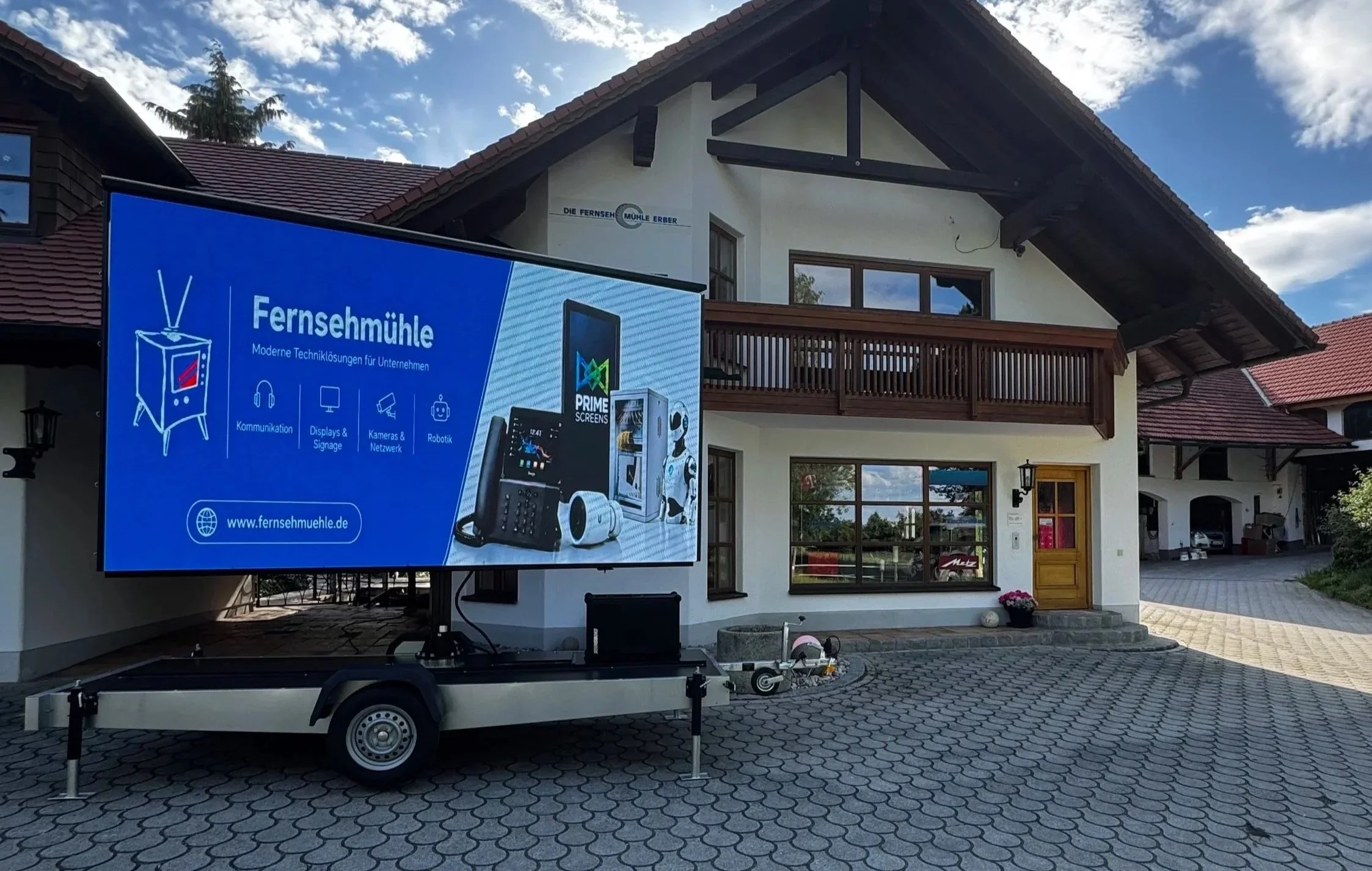 Fahrrad mit mobilem Bildschirm zeigt eine Präsentation über moderne Technologielösungen für Unternehmen vor einem zweistöckigen Haus mit Balkonen.