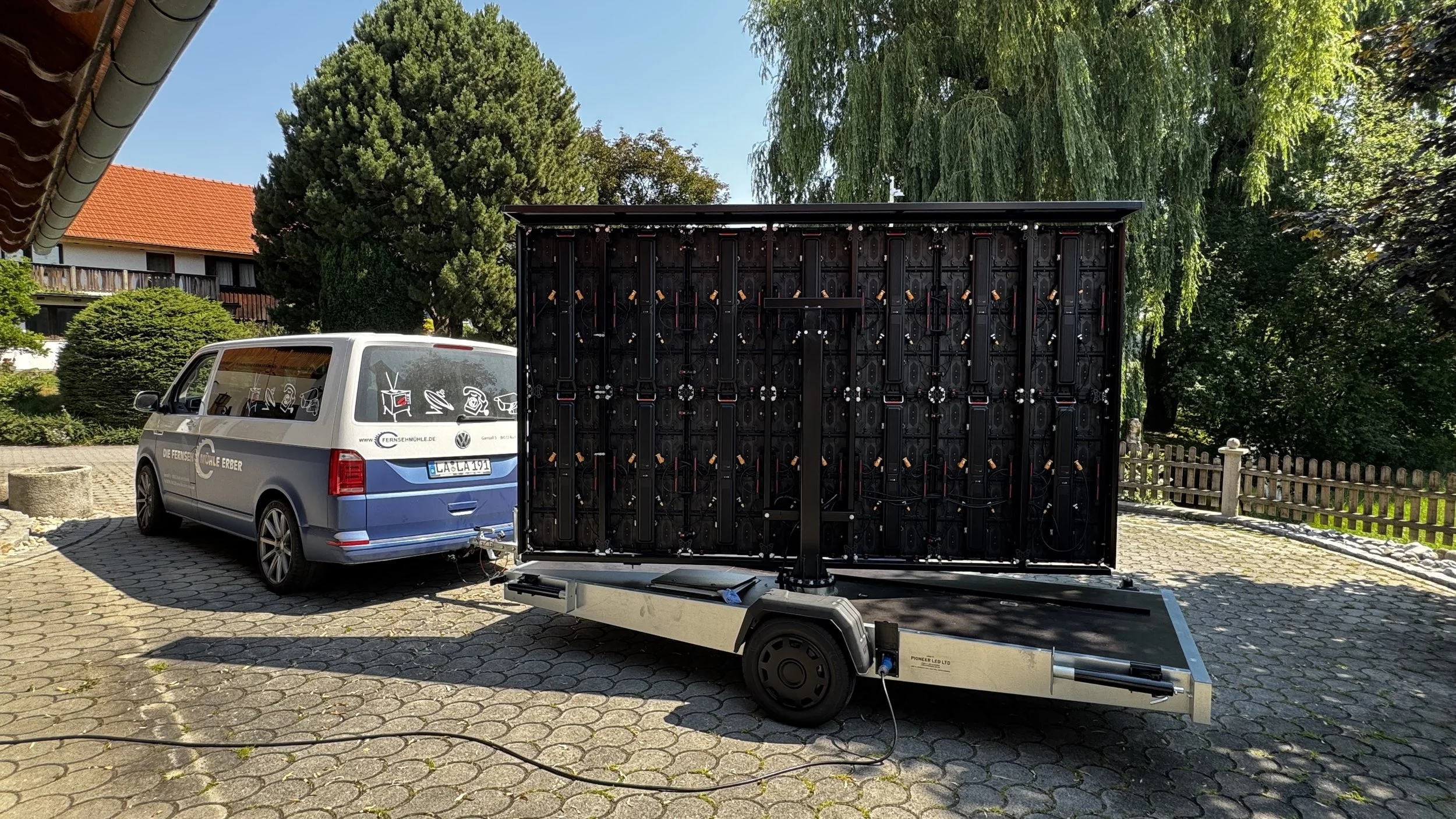 Ein verparkter Van mit Aufschrift 'Die Fernsehmühle Erber' an einem Parkplatz, im Vordergrund ein bewegliches LED-Display mit Skizzen und Kabeln.