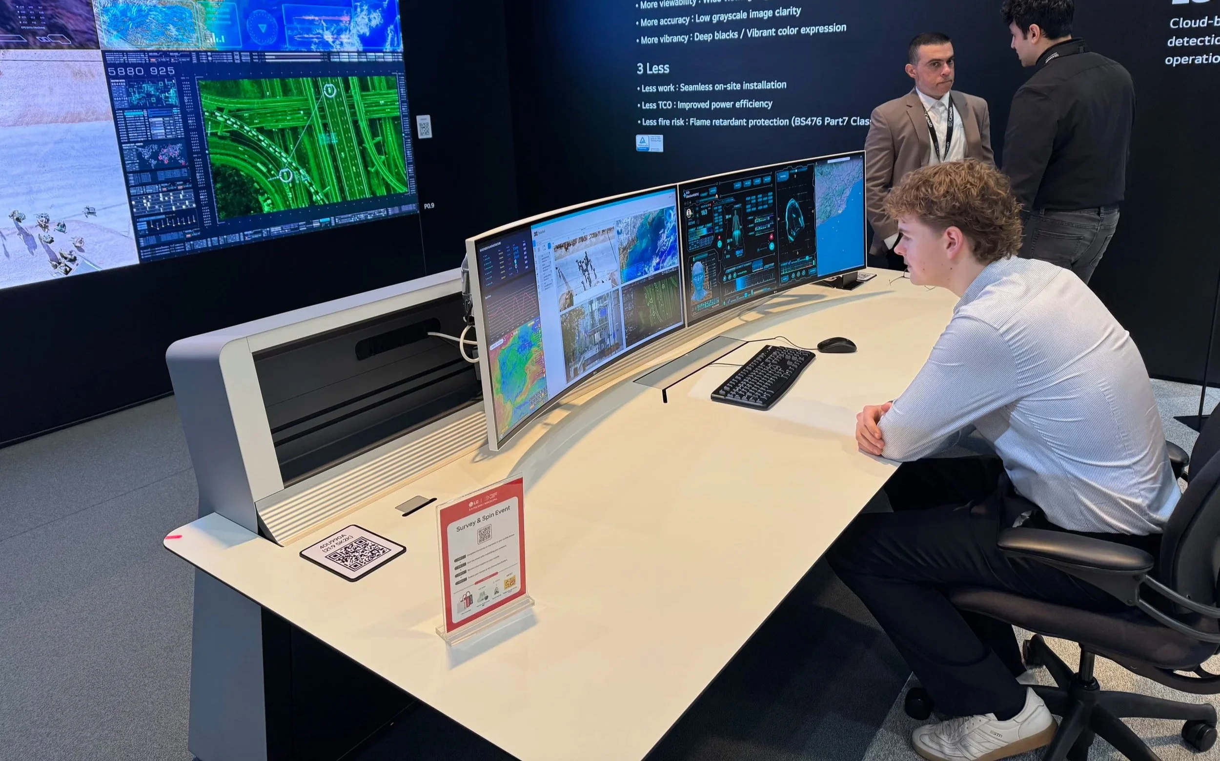 Drei Männer beobachten mehrere Computerbildschirme in einem Kontrollraum, auf denen Karten, Graphen und Daten visualisiert sind.