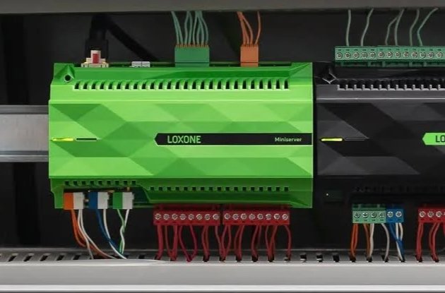 Steuerungspanel mit grüner Loxone Miniserver und verbundenen Kabeln in einem Schaltschrank.