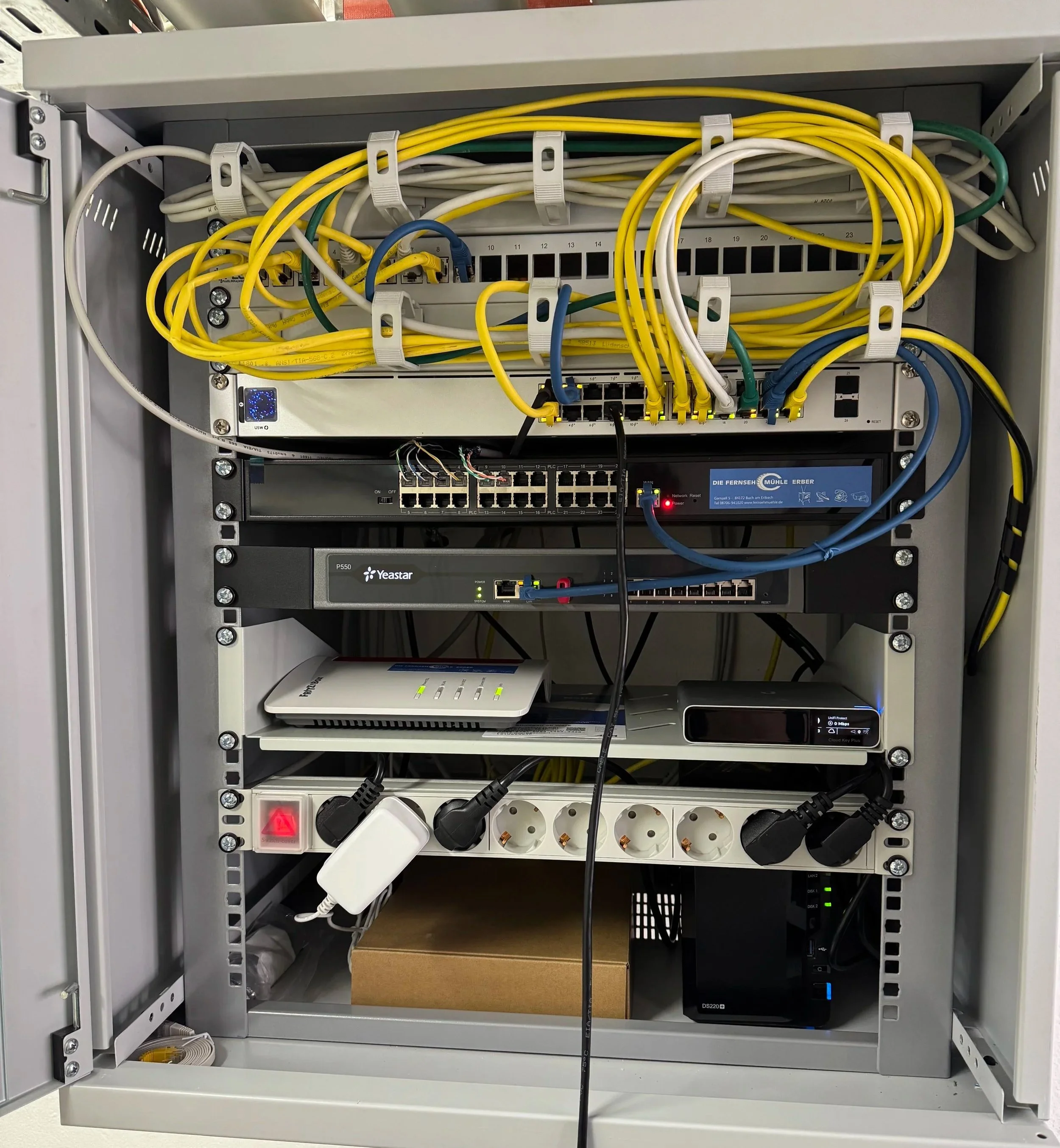 Ein offener Netzwerkschrank mit mehreren Kabeln, Switches und Routern, in einem Technikraum