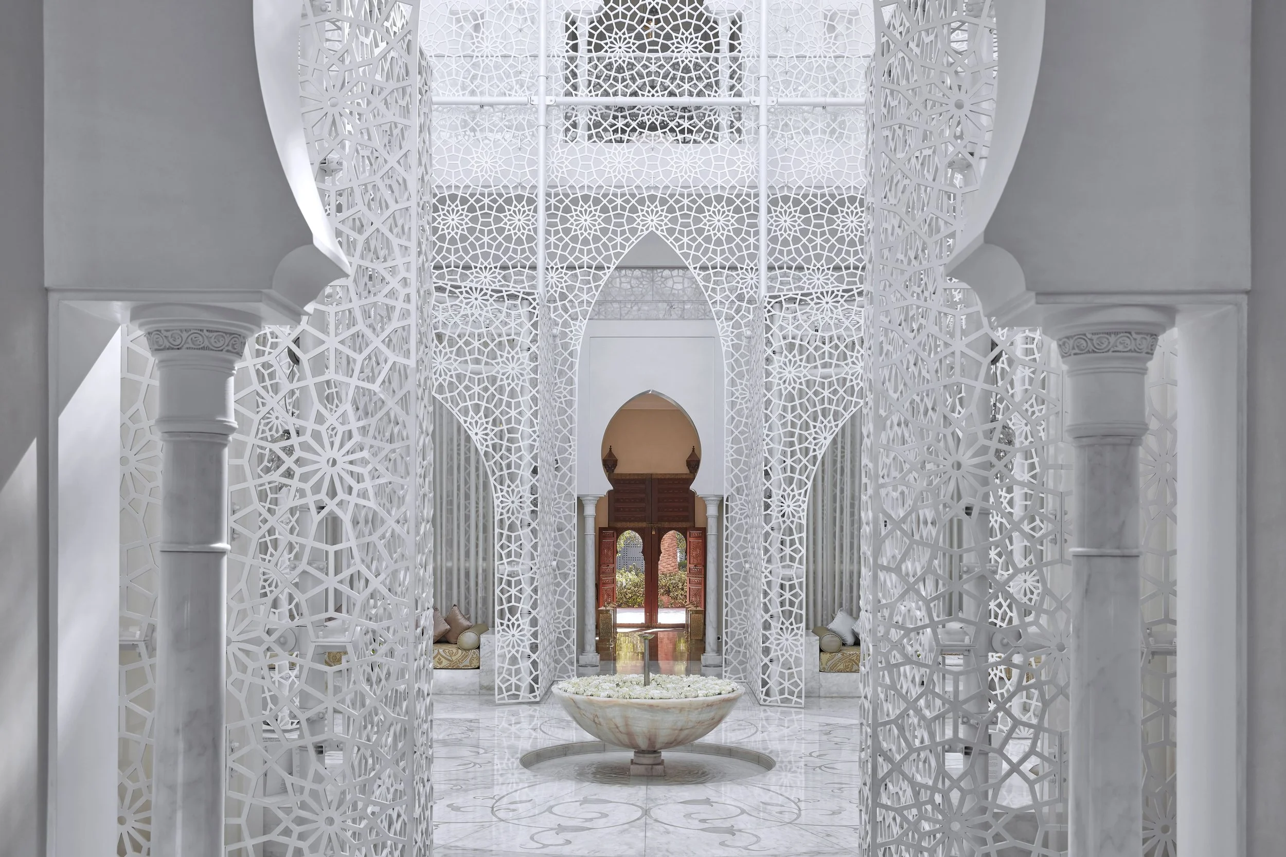 Intricate white geometric lattice screens in a hallway with double doors and a small fountain in the center.
