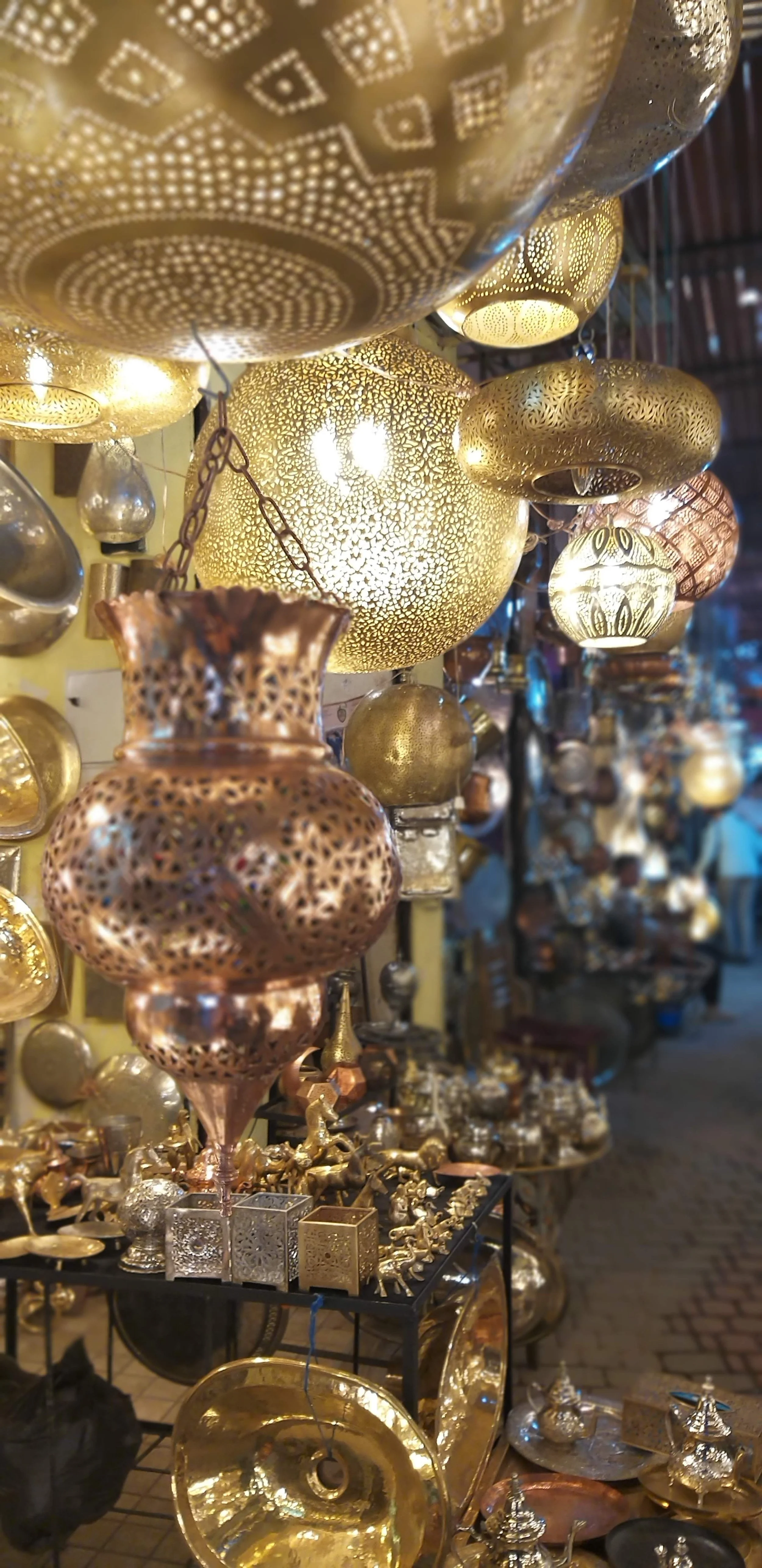 Display of gold and bronze decorative lamps and metalware at a marketplace.