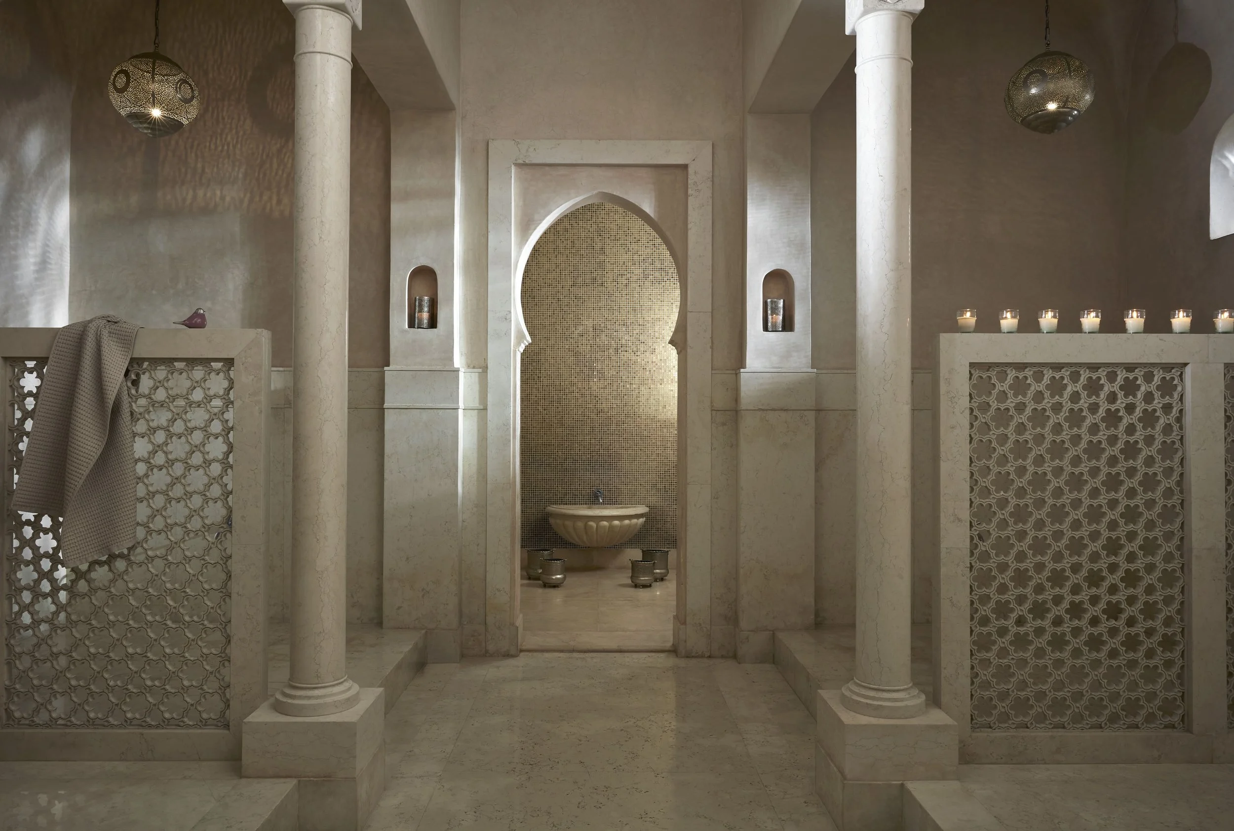 An elegant indoor space with white marble columns and ornate partitions, decorated with multiple candles and intricate lighting fixtures.