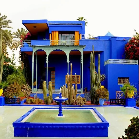 Colorful blue house with cactus garden and fountain in front.