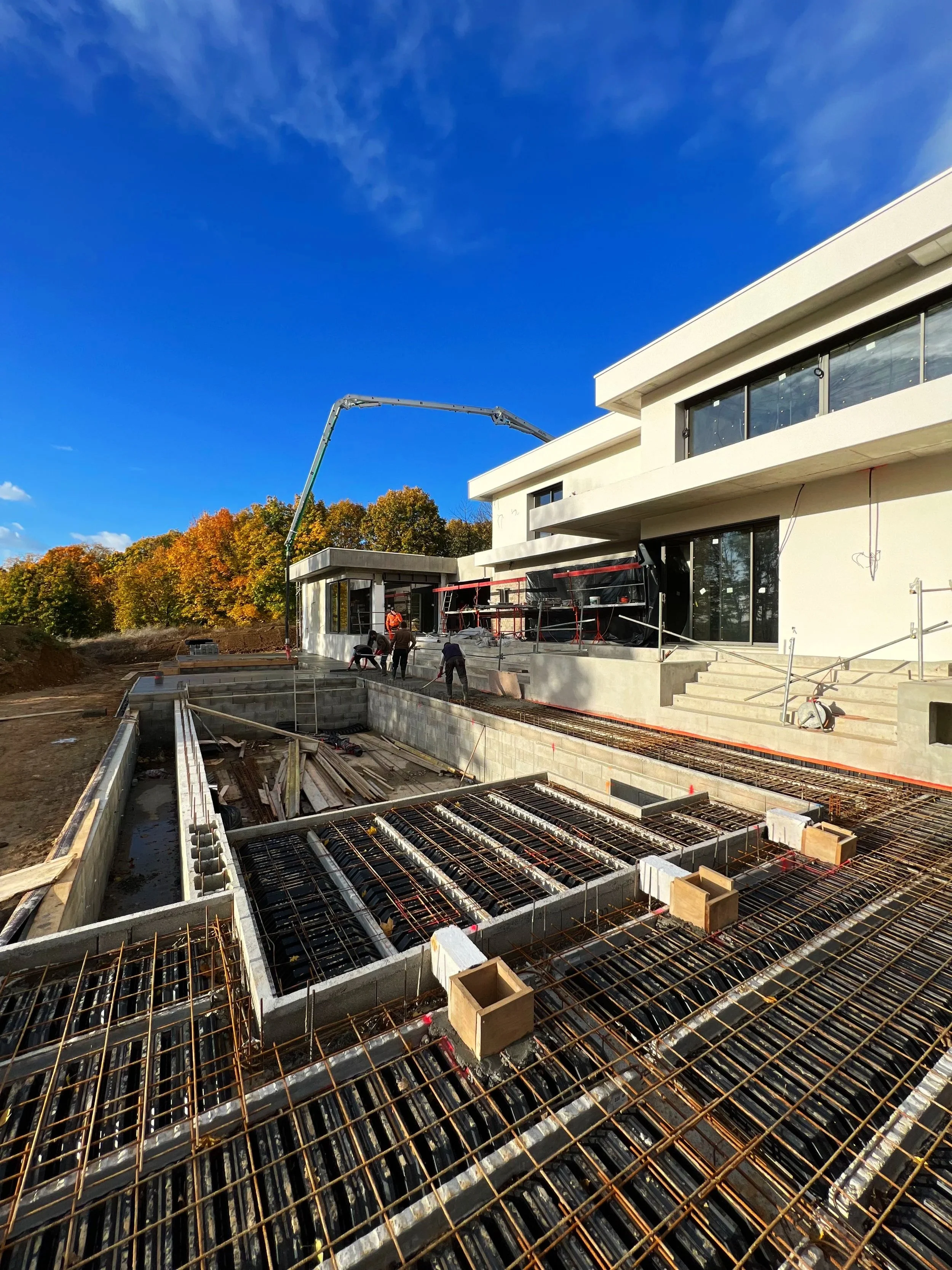 Construction d'une maison moderne avec un ciel bleu clair, des travailleurs et une structure en béton avec du ciment.
