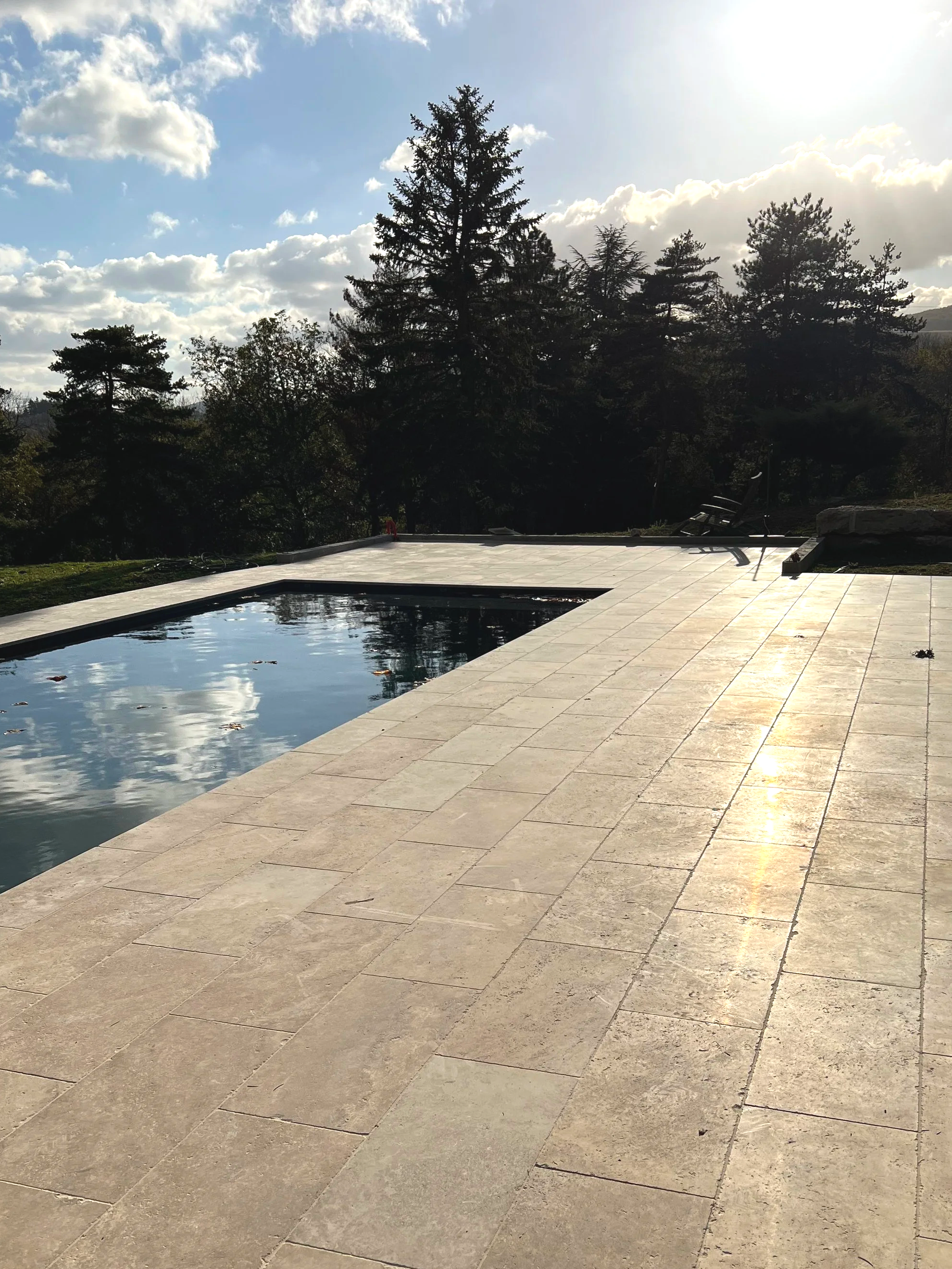 Une piscine en pierre avec une vue sur un ciel partiellement nuageux et des arbres en arrière-plan, sous la lumière du soleil