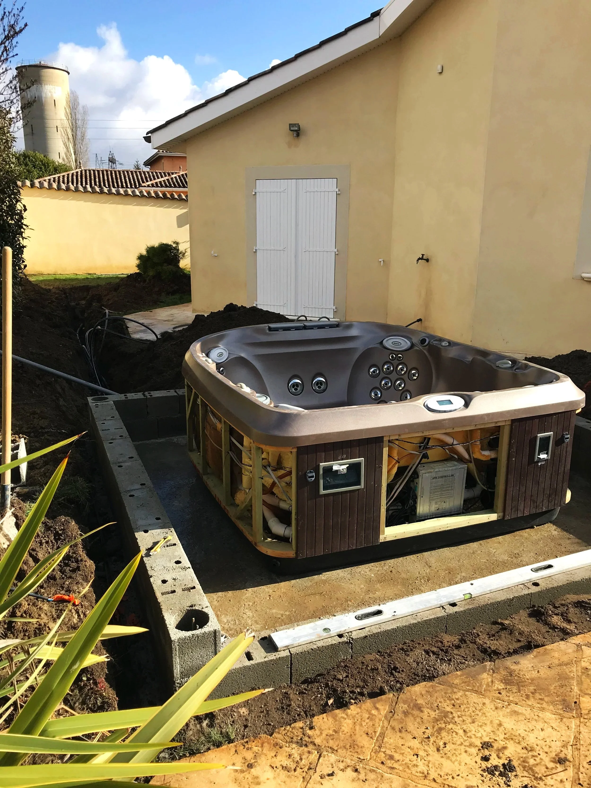 Installation d'un spa extérieur en construction près d'une maison avec des murs jaunes, des outils et des matériaux de construction autour.
