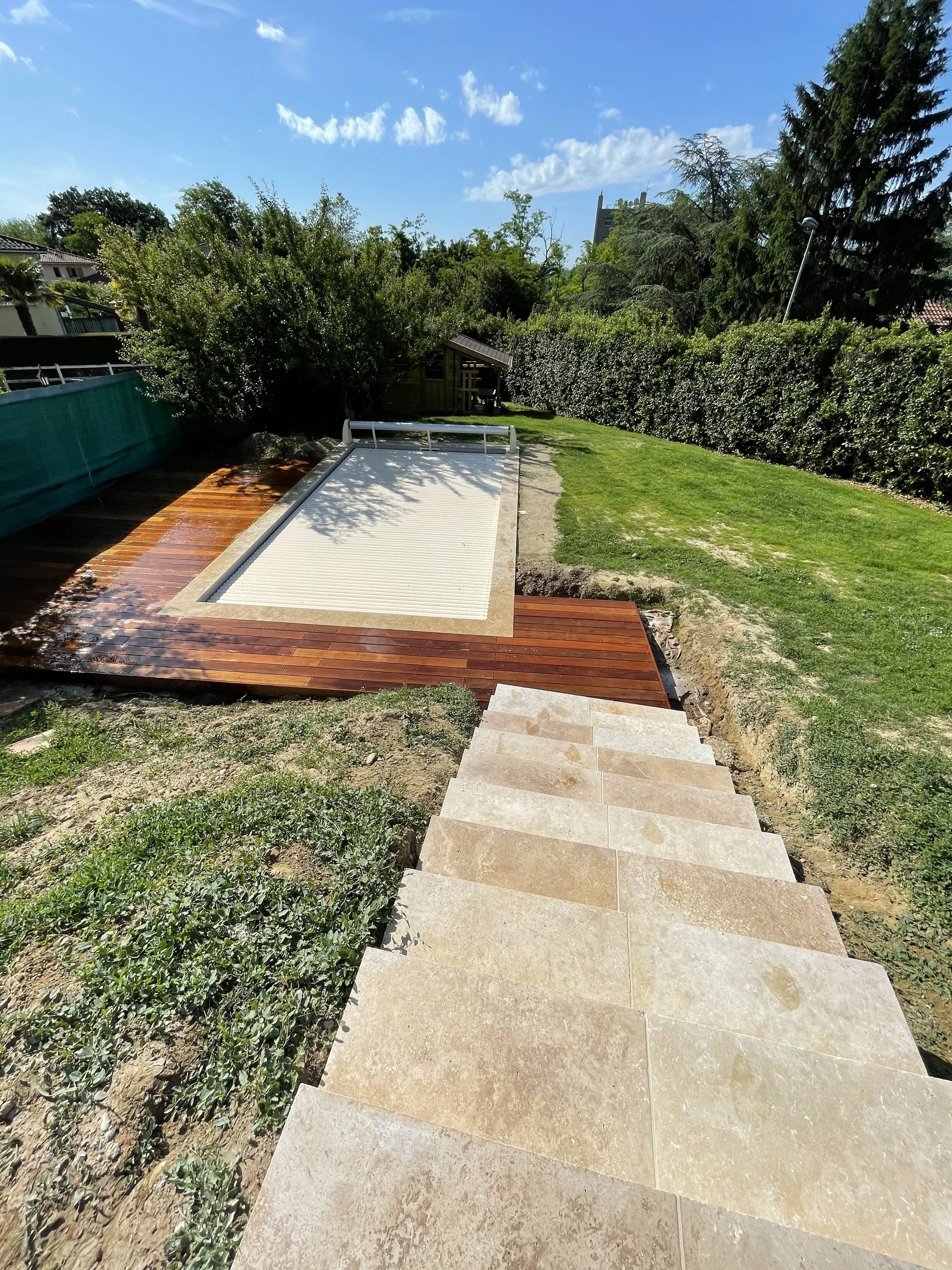 Escalier en pierre menant à un espace extérieur avec pelouse, arbres et un petit bâtiment en bois dans un jardin ensoleillé.