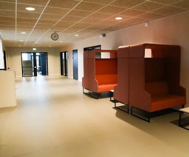 Ett tomt väntrum eller lobby med två orangea sittplatser med höga väggar och en väckklocka på taket.