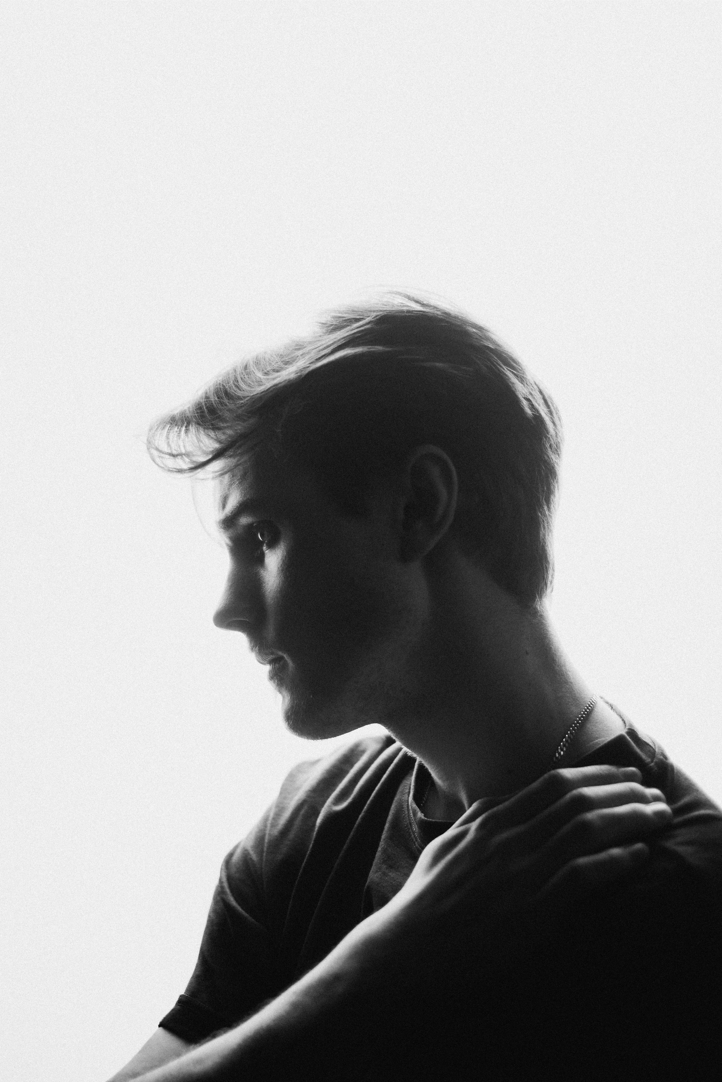 Svartvit bild av en person i profil, med kort hår och en kedja runt halsen, avkopplad med armar korsade.
