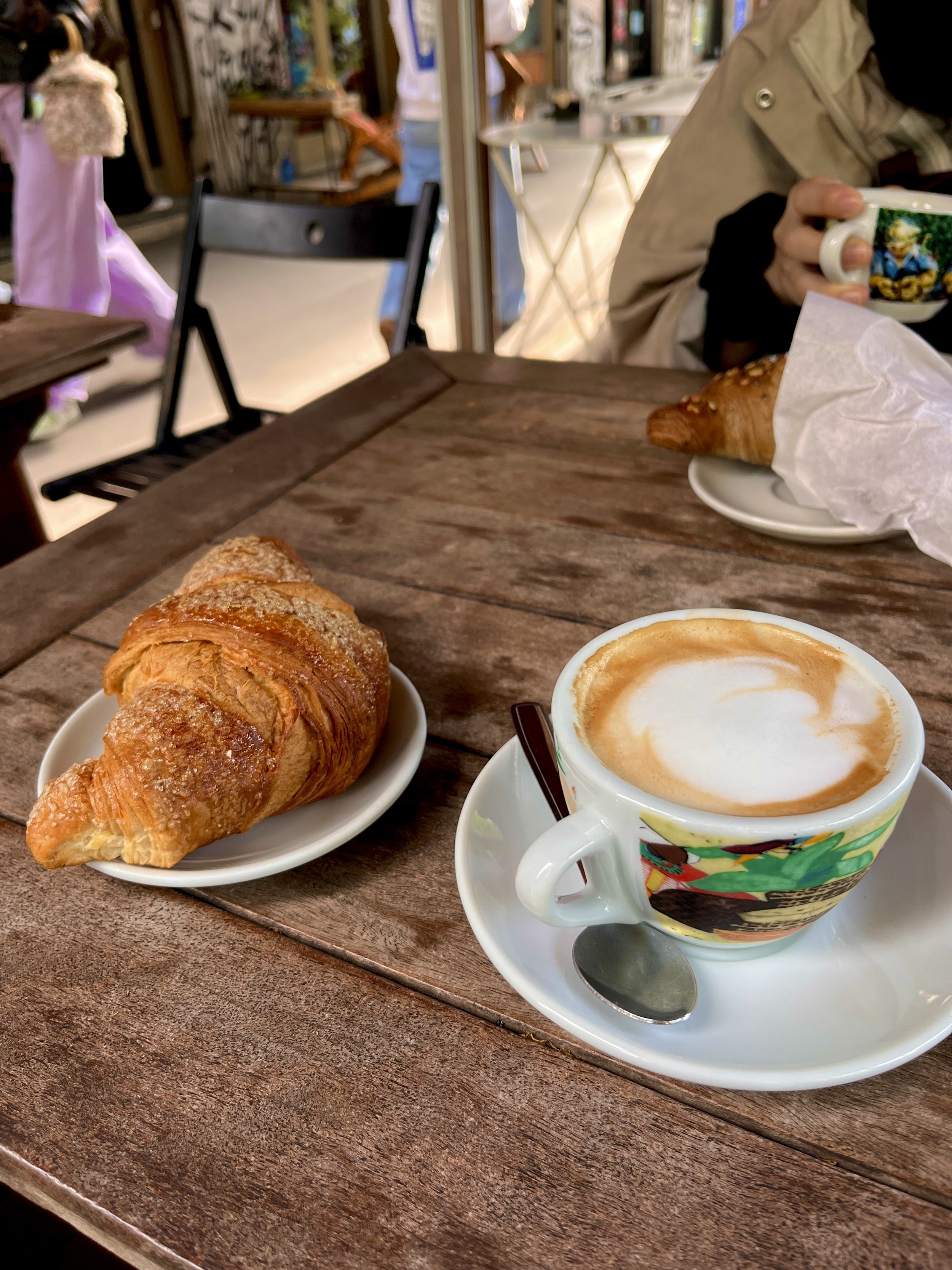 A cappuccino and two croissants on a table outside a cafe in italy