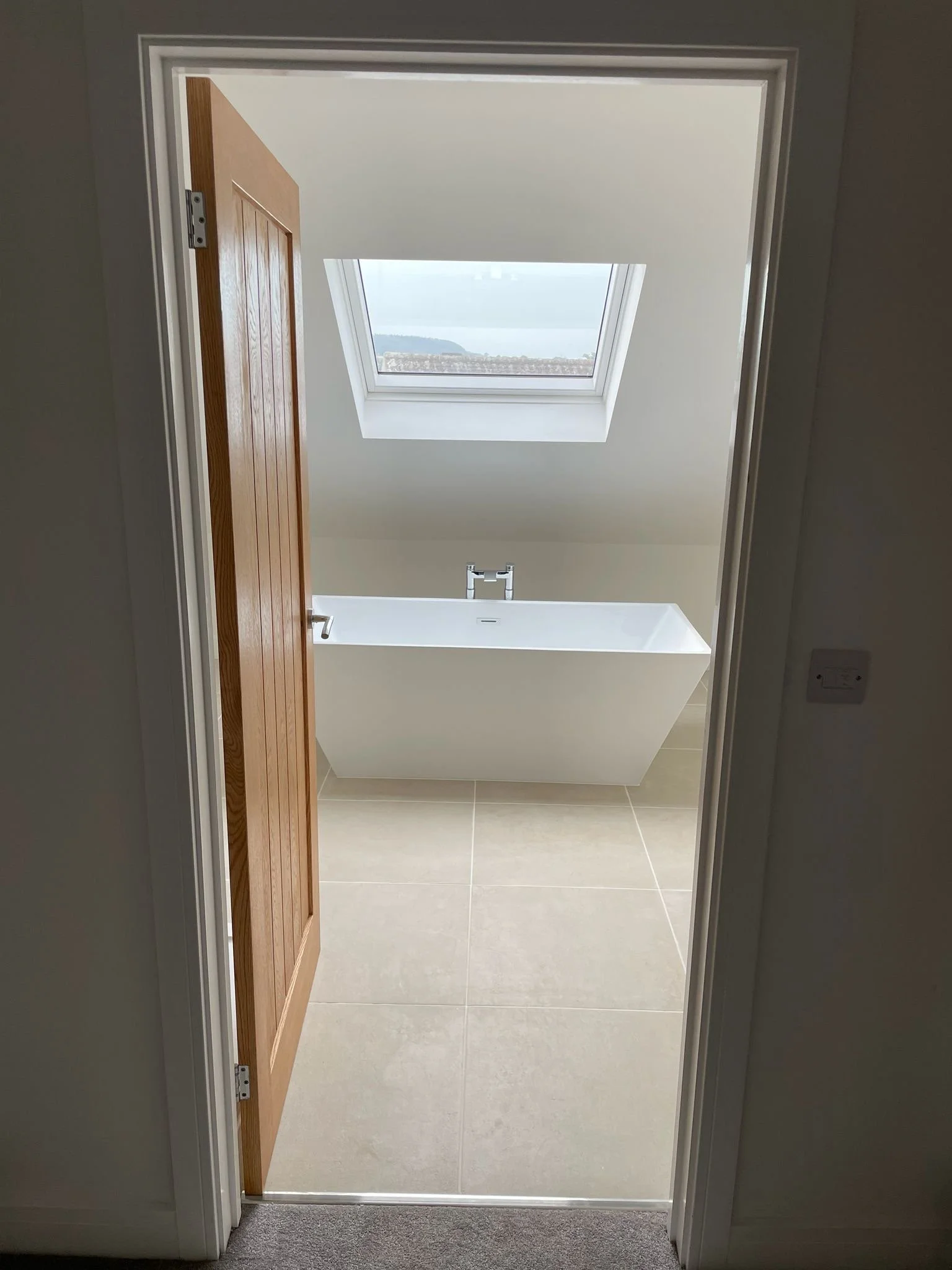View through an open wooden door into a room with a skylight window showing a landscape with water and distant land.