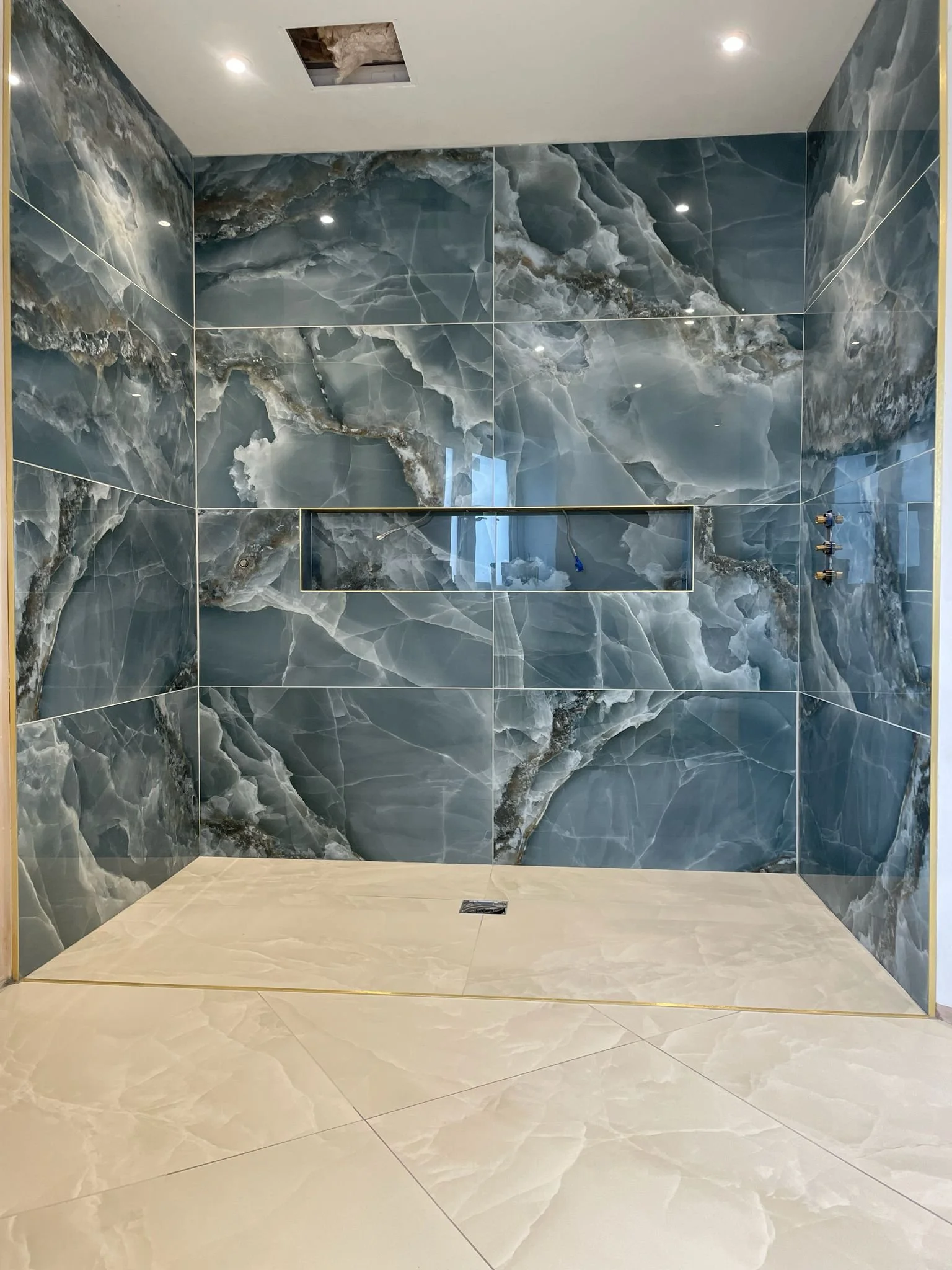 A modern shower with blue and white marble tiles, a built-in niche, and a light-colored tiled floor.