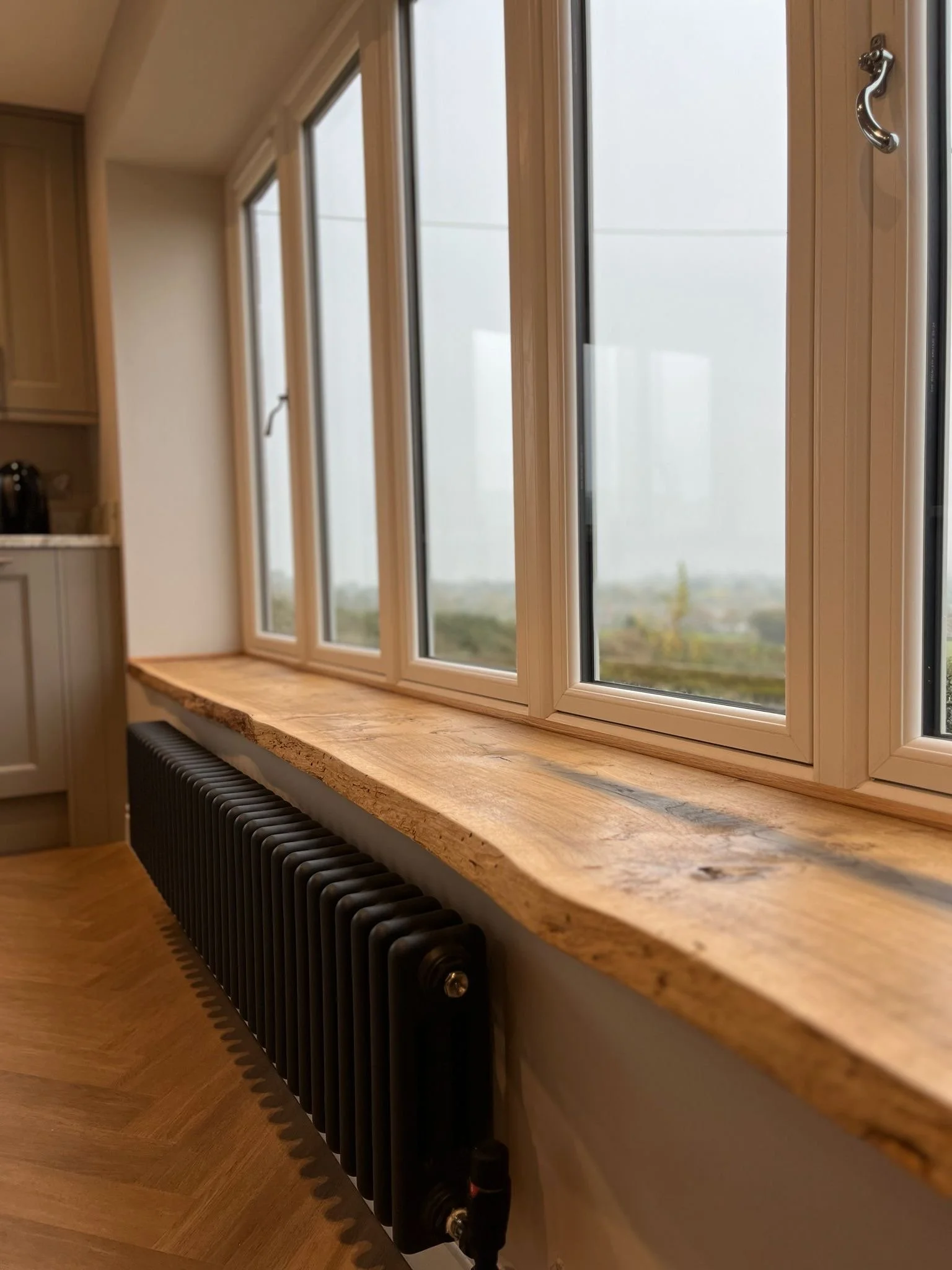 Close-up of a wooden window sill with a black radiator underneath, seen from inside a room with wooden flooring.