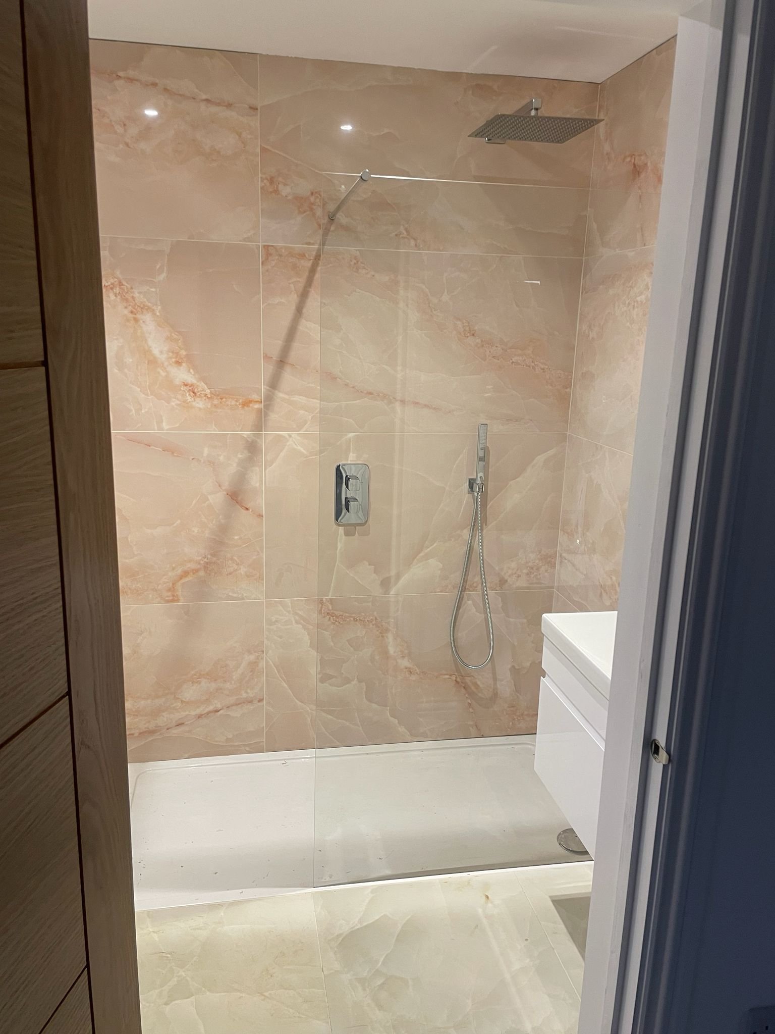 Modern walk-in shower with beige marble tile walls, a large square rainfall showerhead, a handheld showerhead, and a wall-mounted control panel.