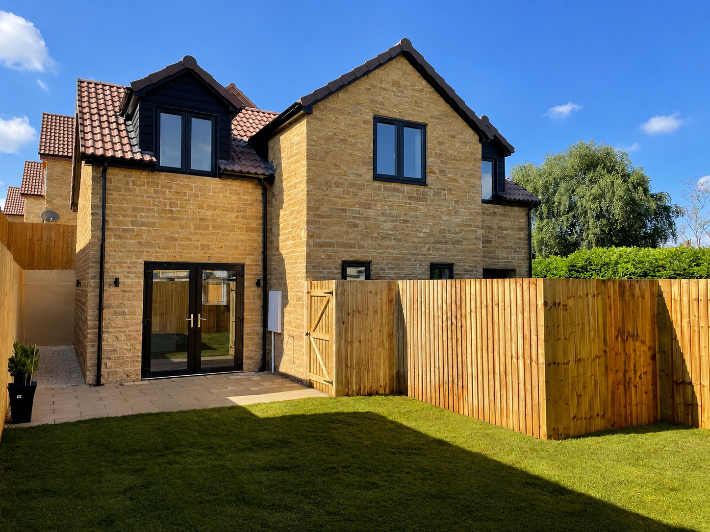 Backyard view of a modern two-story house with brick exterior, black window frames, and a wooden fence, under a clear blue sky.
