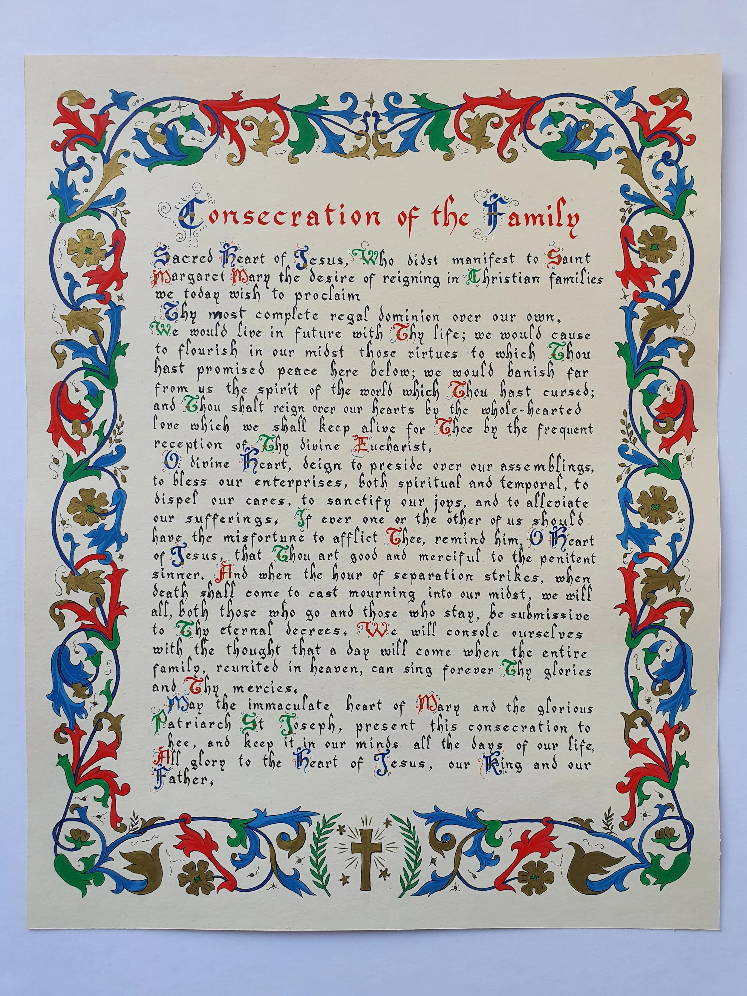 Page de texte calligraphié et enluminée de la prière catholique "Consecration of the family", avec une bordure décorative au motif végétal coloré en rouge, bleu et or.