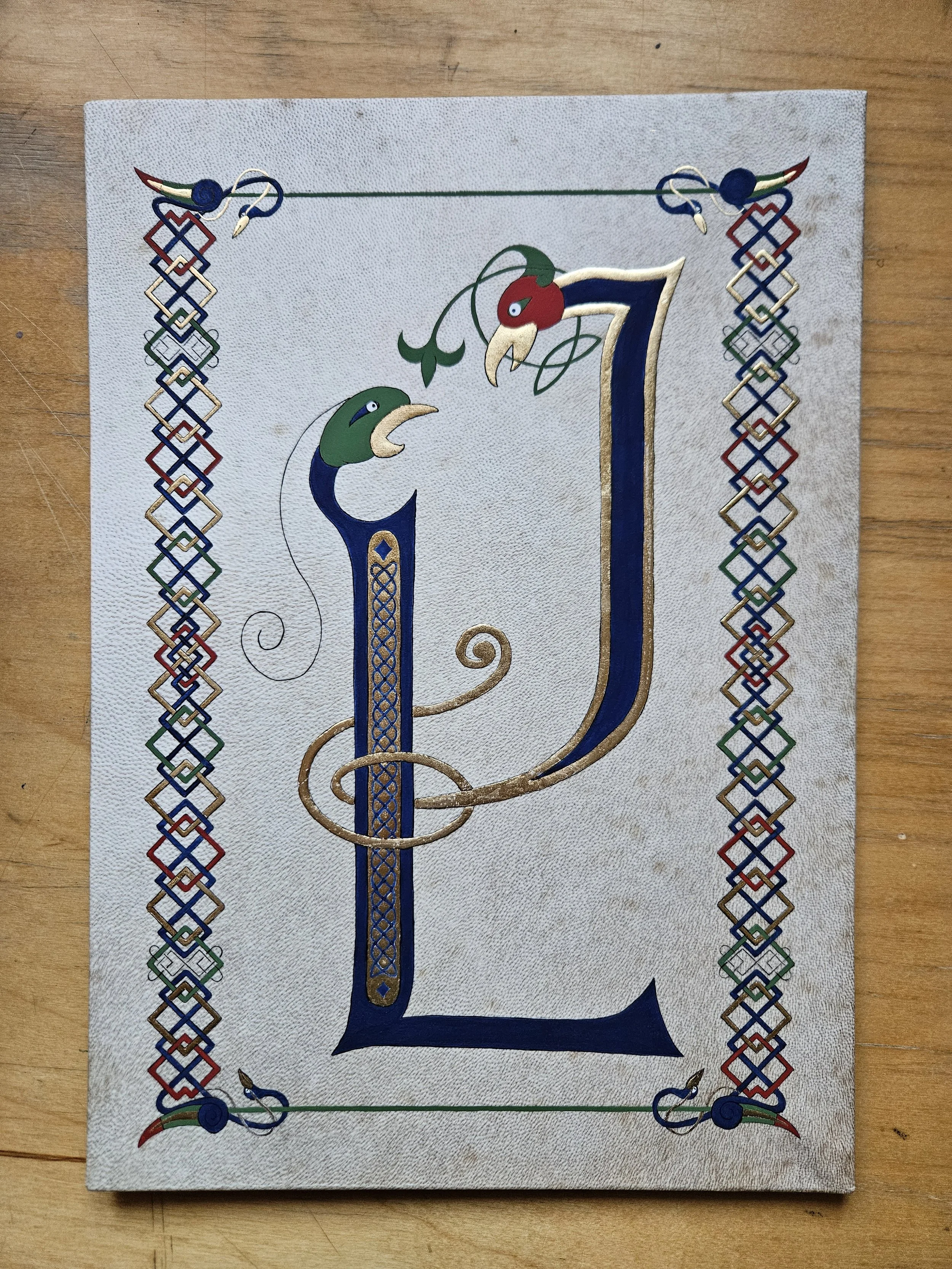 Une illustration médiévale représentant deux grandes lettres en forme d'oiseau, entrelacées et enluminées dans un style celtique, entourées d'une bordure géométrique colorée et dorée à la feuille d'or.