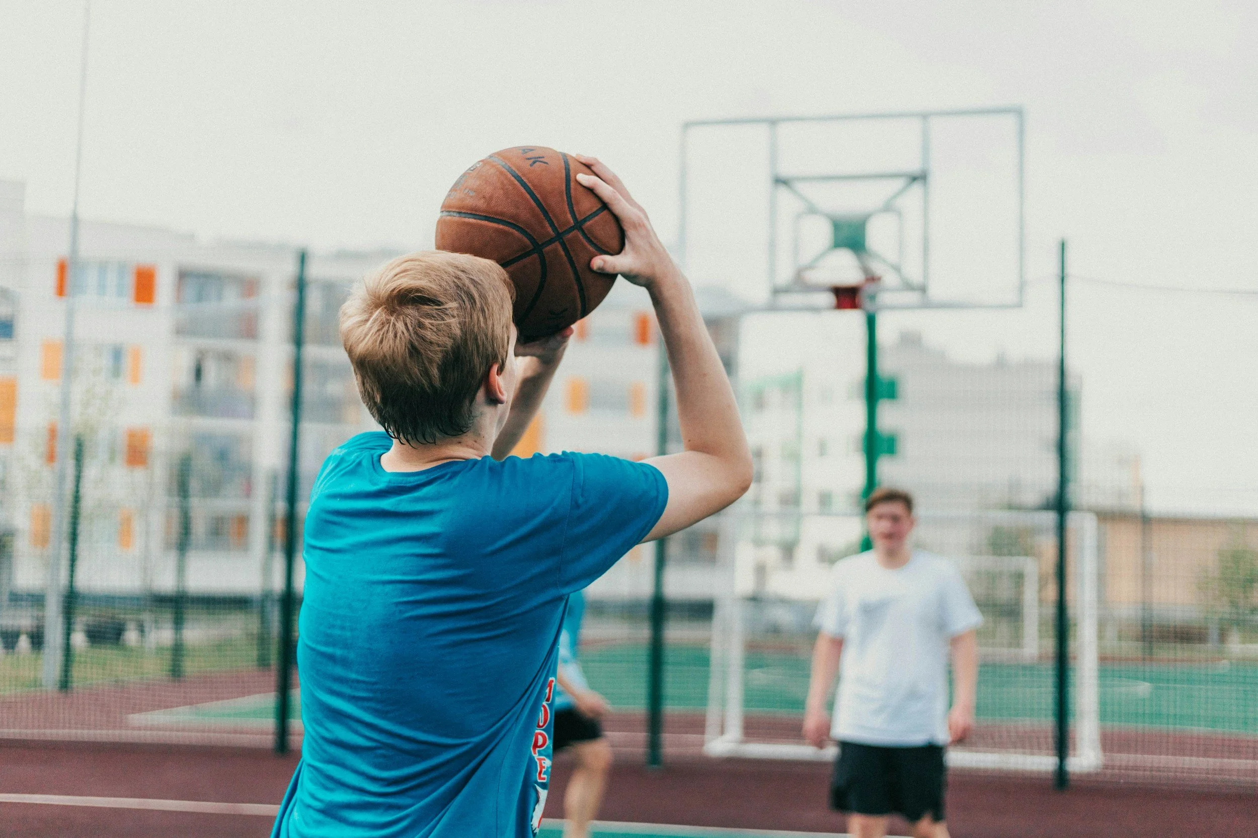 Junge spielt Basketball auf einem Outdoor-Sportplatz.