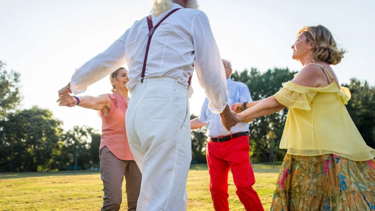 Menschen im Freien, die sich beim Tanzen im Kreis halten, bei Sonnenuntergang, fröhliche Atmosphäre, Momente des Zusammenlebens und der Freude.